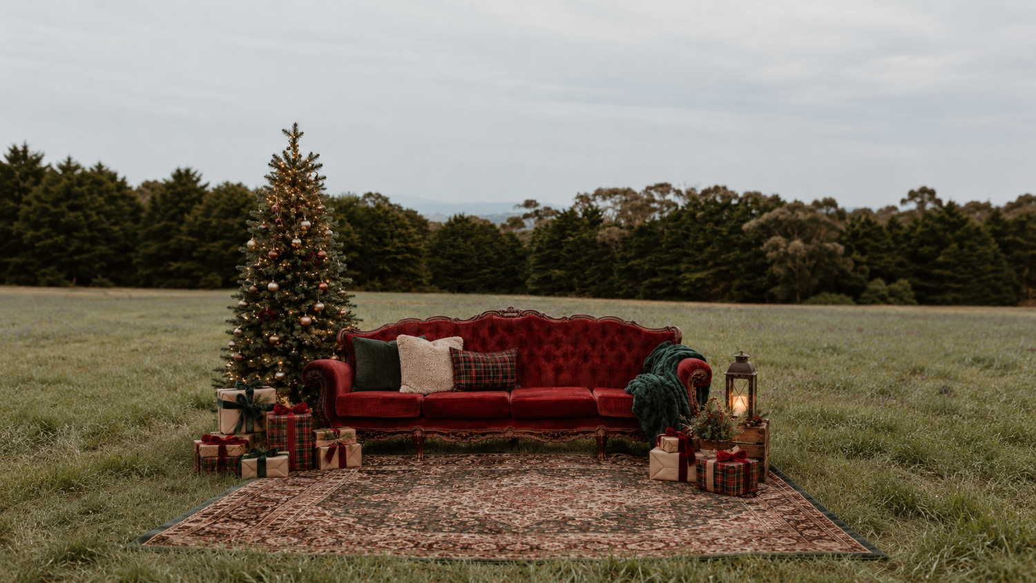 Red velvet sofa with Christmas tree, gifts, and lantern on a rug in an open field holiday outdoor setting.