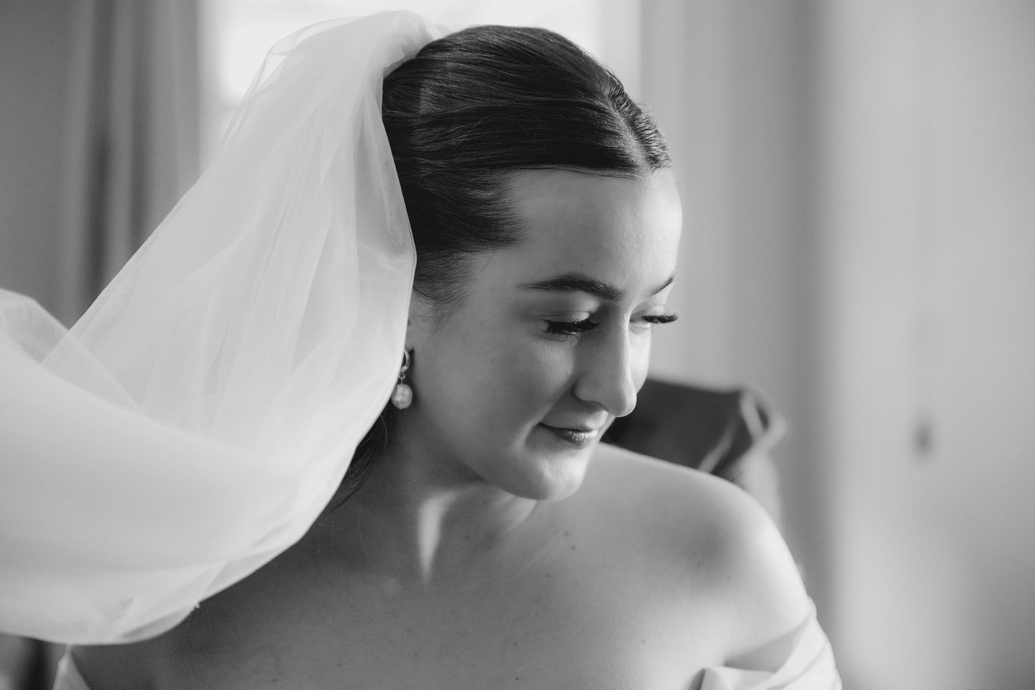 A bride in a white wedding gown and veil smiles while getting ready for her wedding ceremony.