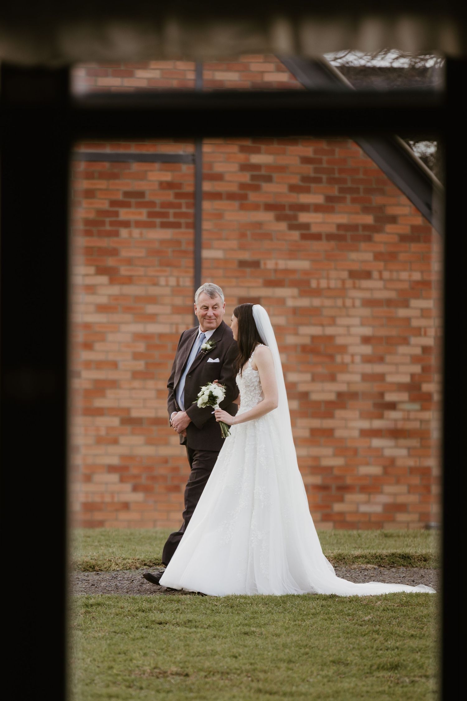 A wedding moment viewed through a window frame with a brick wall backdrop.