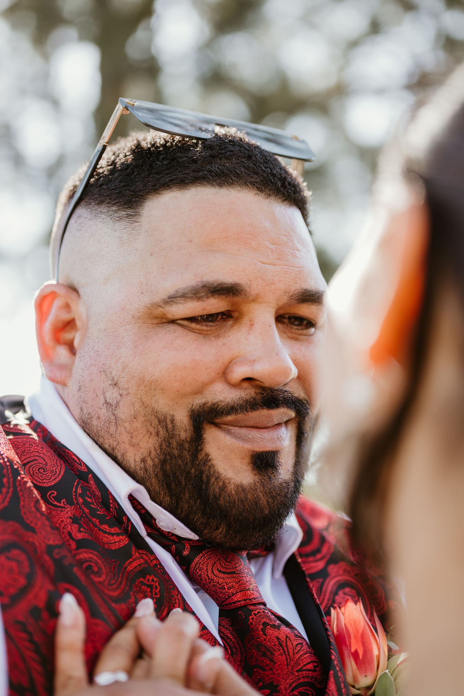 Close-up profile view of someone wearing a red paisley patterned vest and white dress shirt.