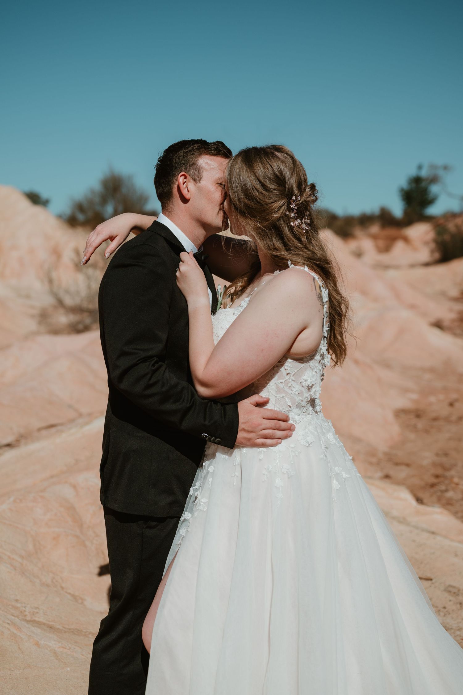 Romantic wedding kiss against desert landscape and blue sky.