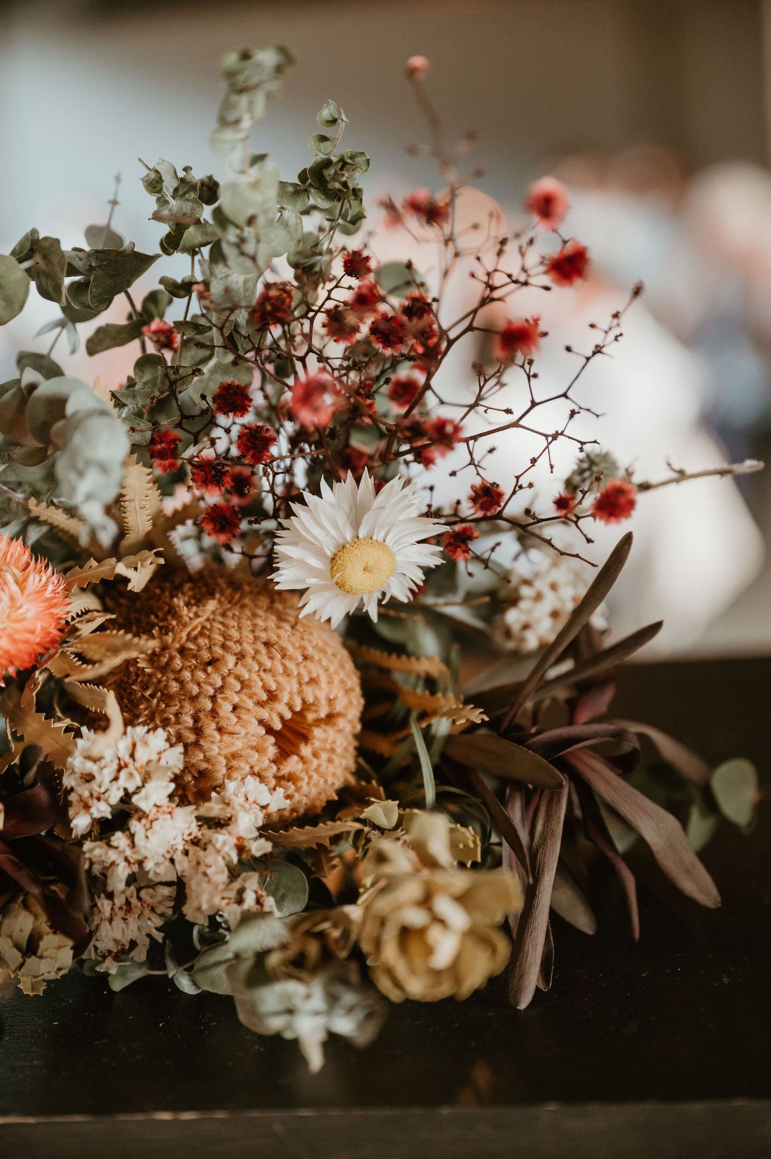 An artistic wedding flower arrangement featuring daisies and red berries in moody lighting.
