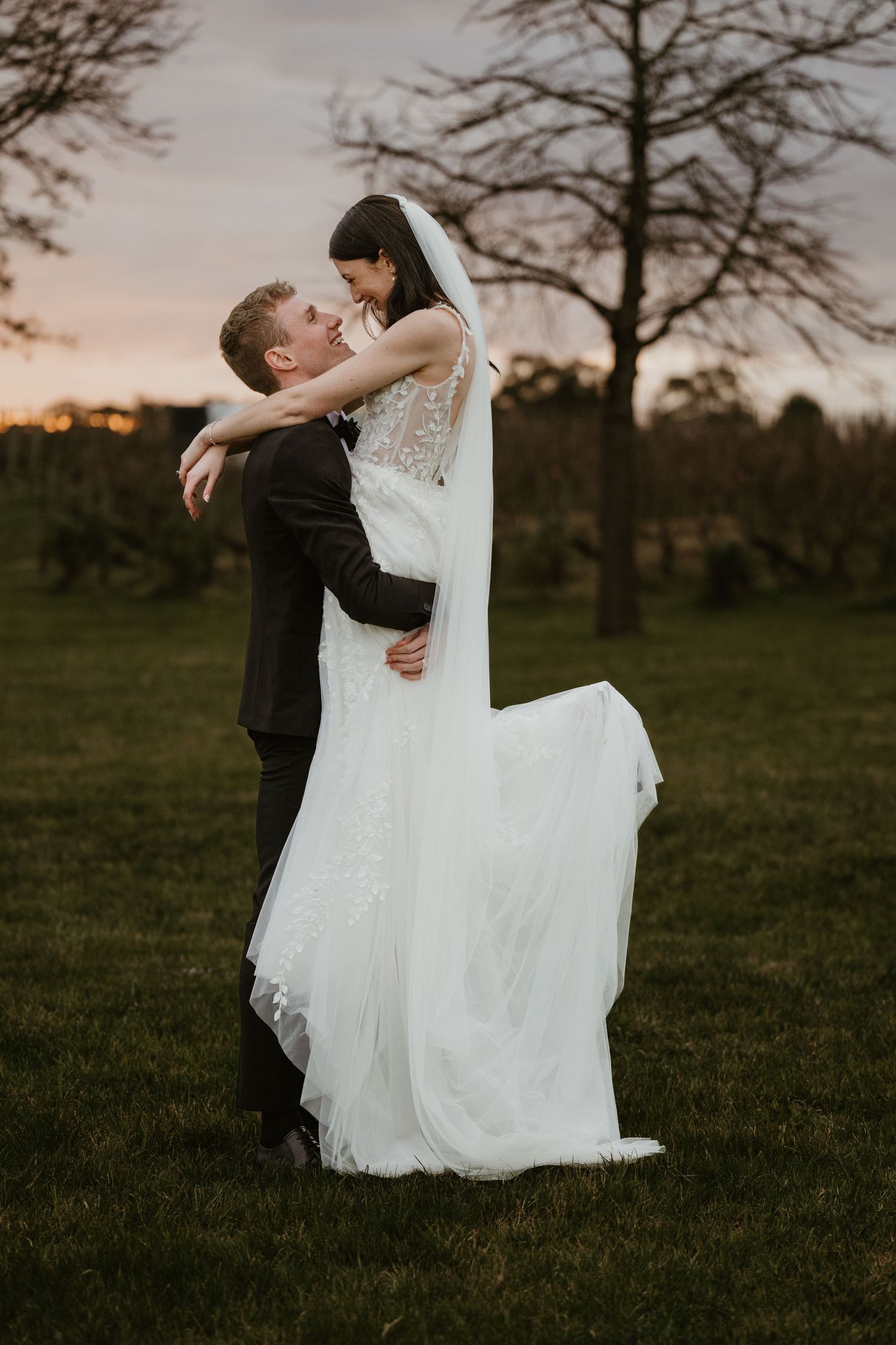 A romantic moment captured as the groom lifts his bride in a flowing white dress at sunset.