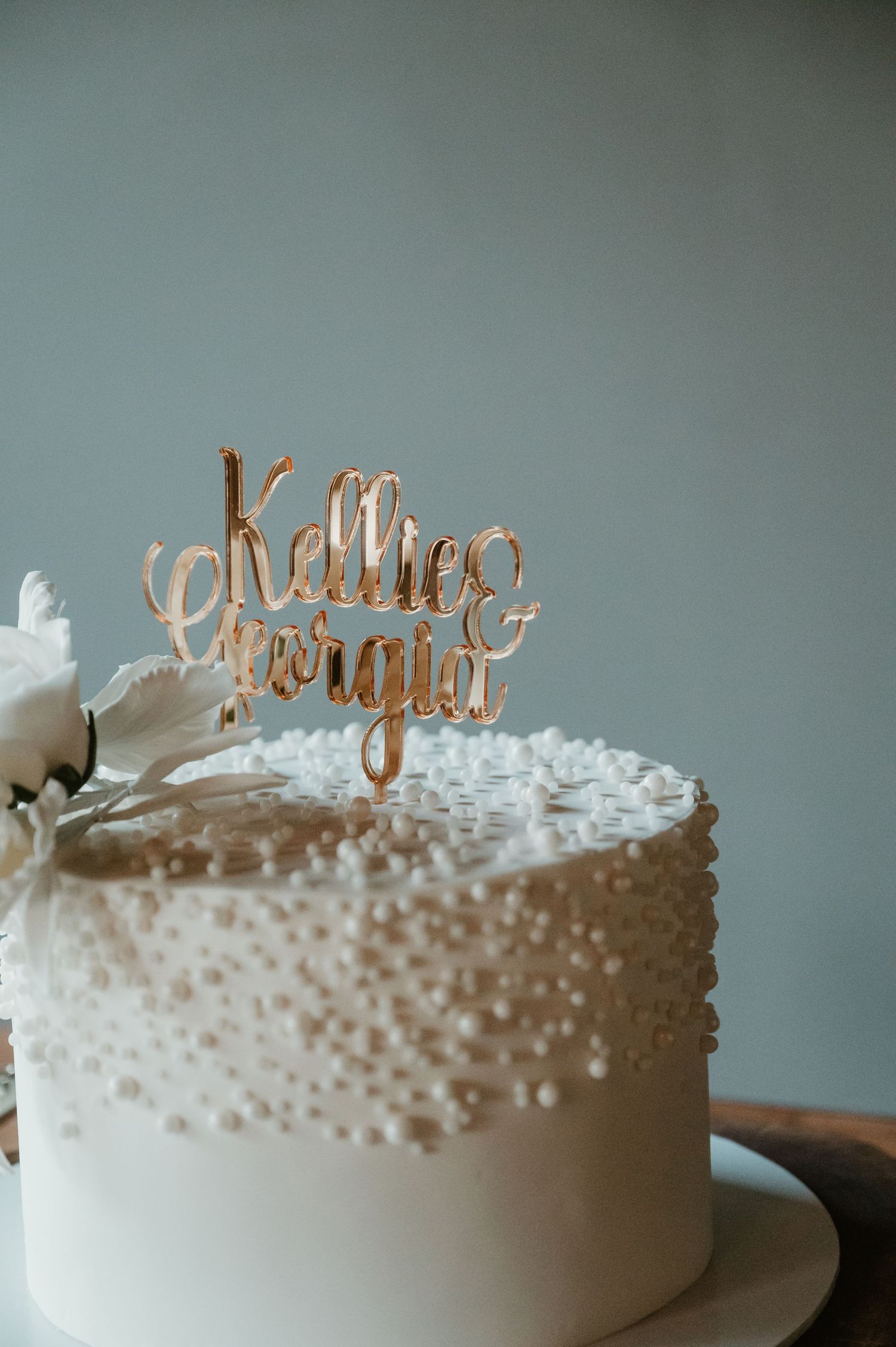 A white wedding cake decorated with pearl-like dots and gold text topper.