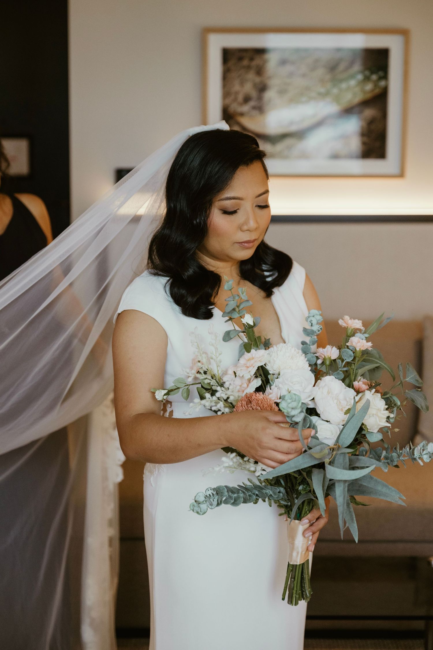 A bride in an elegant white dress holds a beautiful bouquet featuring white flowers and eucalyptus leaves.