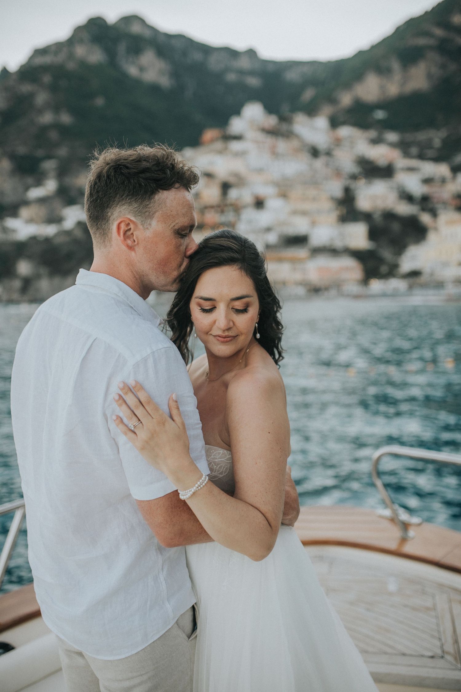 A tender moment shared on a wooden boat with the Amalfi Coast's stunning backdrop.