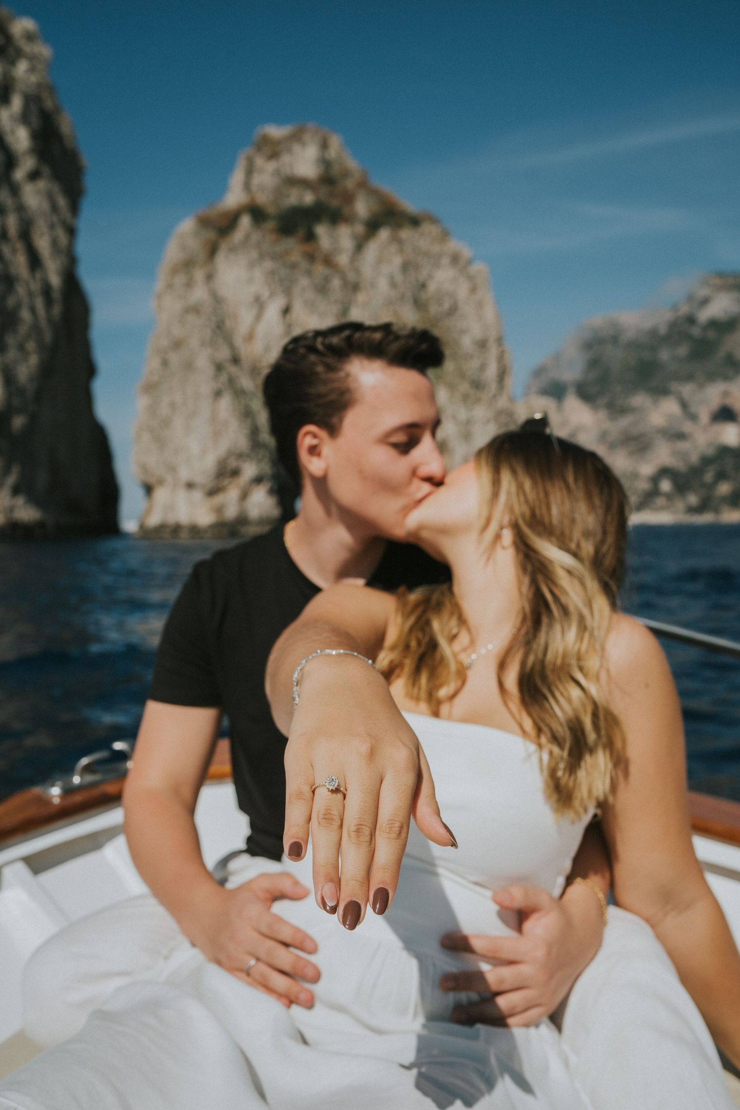 A couple celebrates their engagement on a boat with Capri's famous rocks in background.