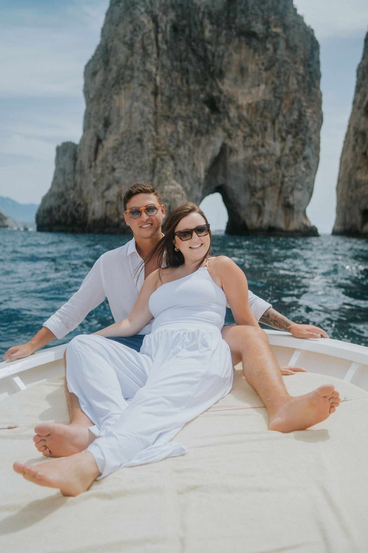 A relaxed couple lounges on a boat deck near the famous Faraglioni rocks of Capri.