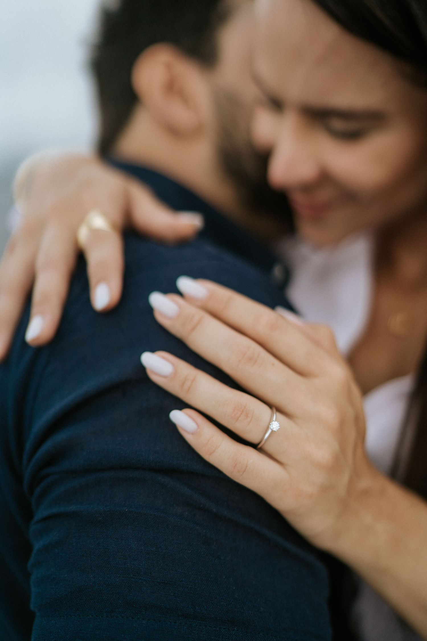 A close-up shot of hands with an engagement ring against formal attire.