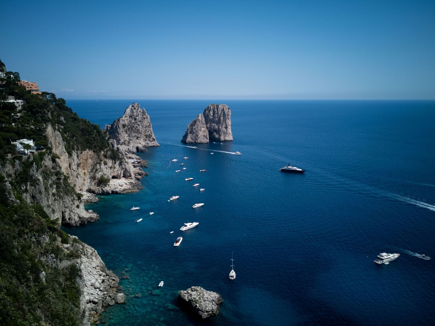 Dramatic coastal landscape showing boats anchored near towering limestone cliffs against azure waters.
