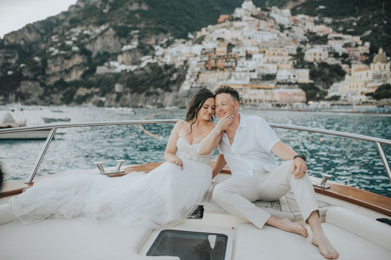 Couple relaxing on a luxury yacht deck overlooking a scenic coastal landscape with mountains in the background.