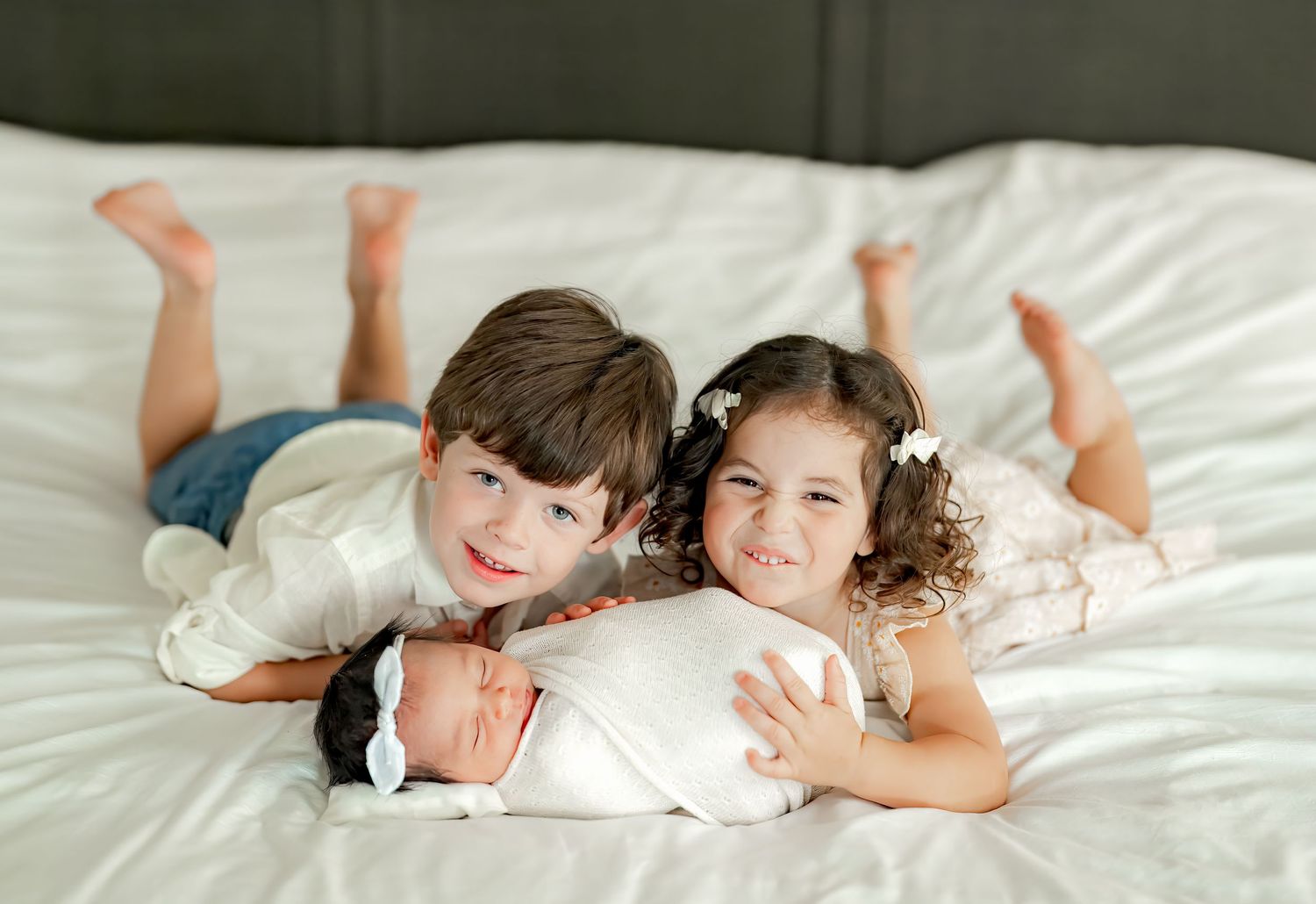 Two children lying on white bedding while looking at something together.