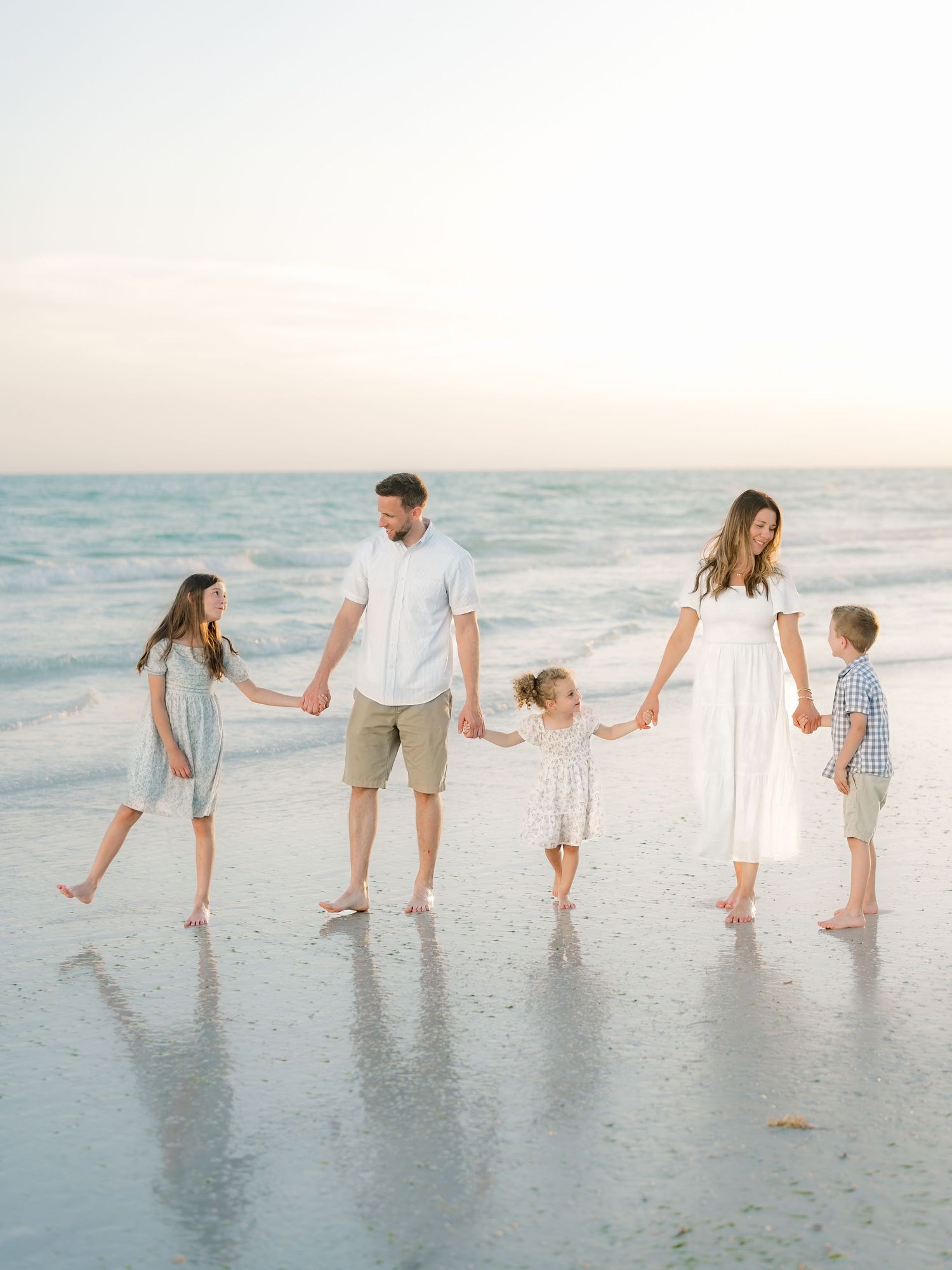 Family holding hands while walking together on a beach at sunset.