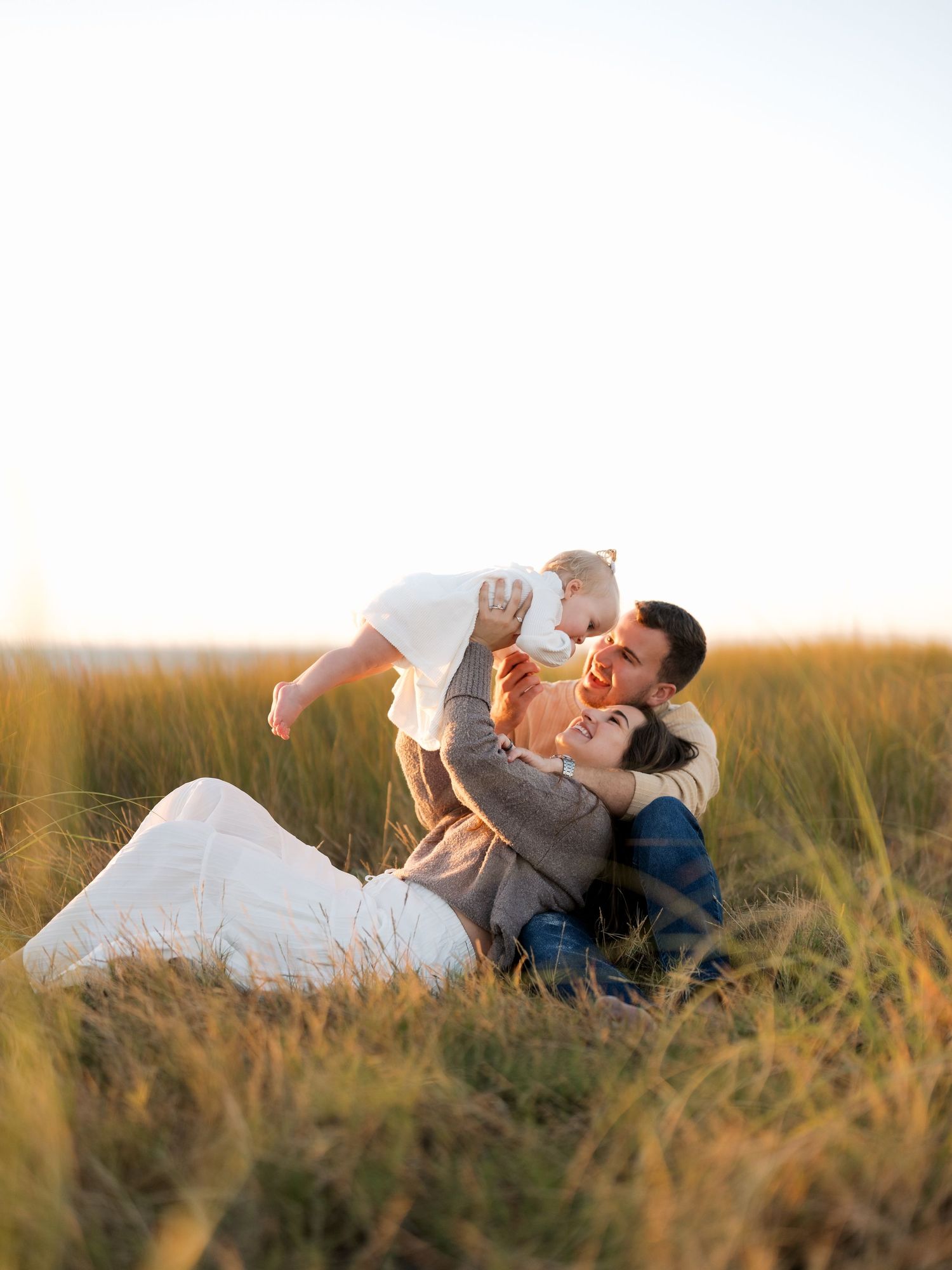 Couple lying in tall grass during golden hour sharing intimate moments together in a romantic outdoor setting.