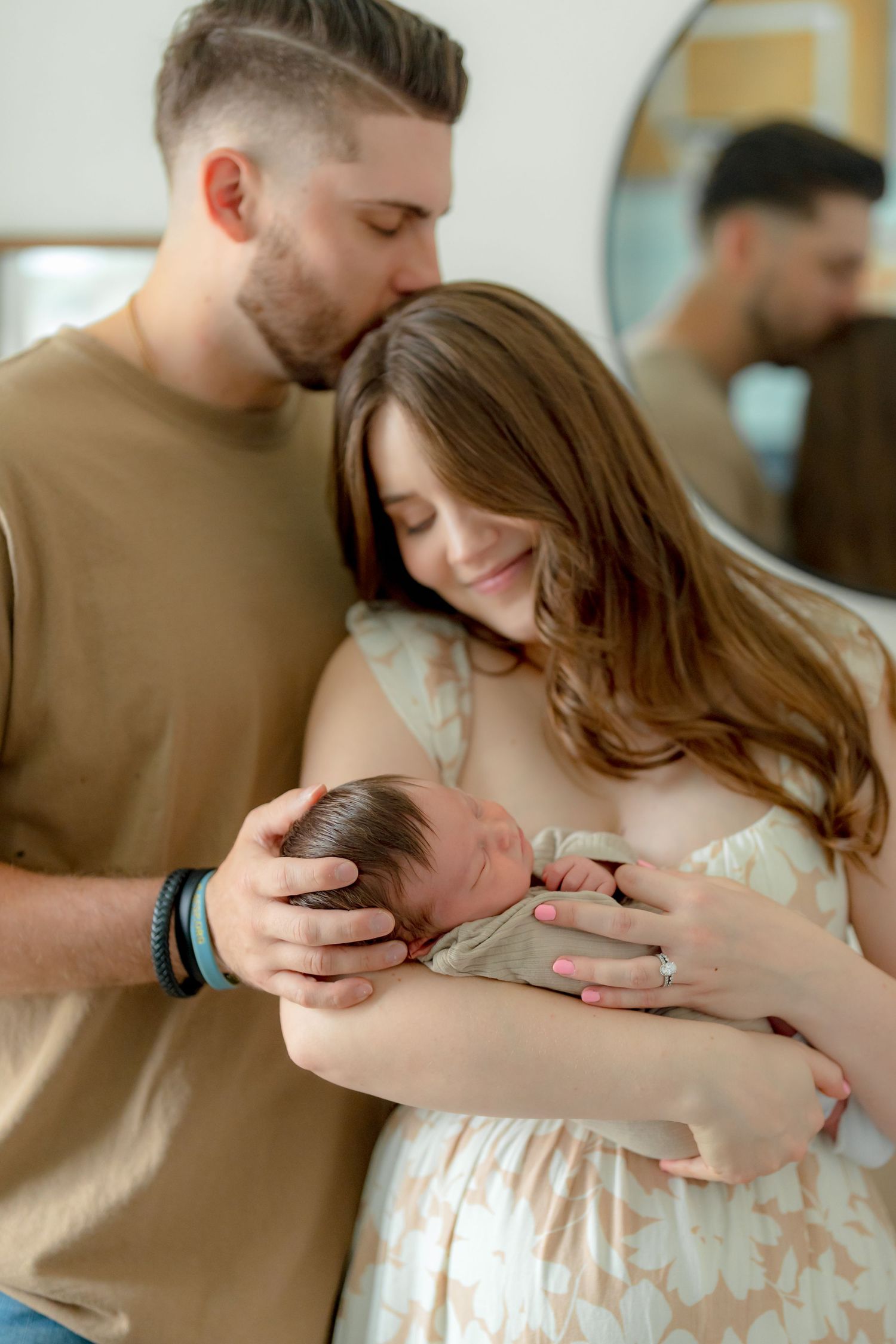 Parents sharing a tender moment while holding their newborn baby in a sunny room.