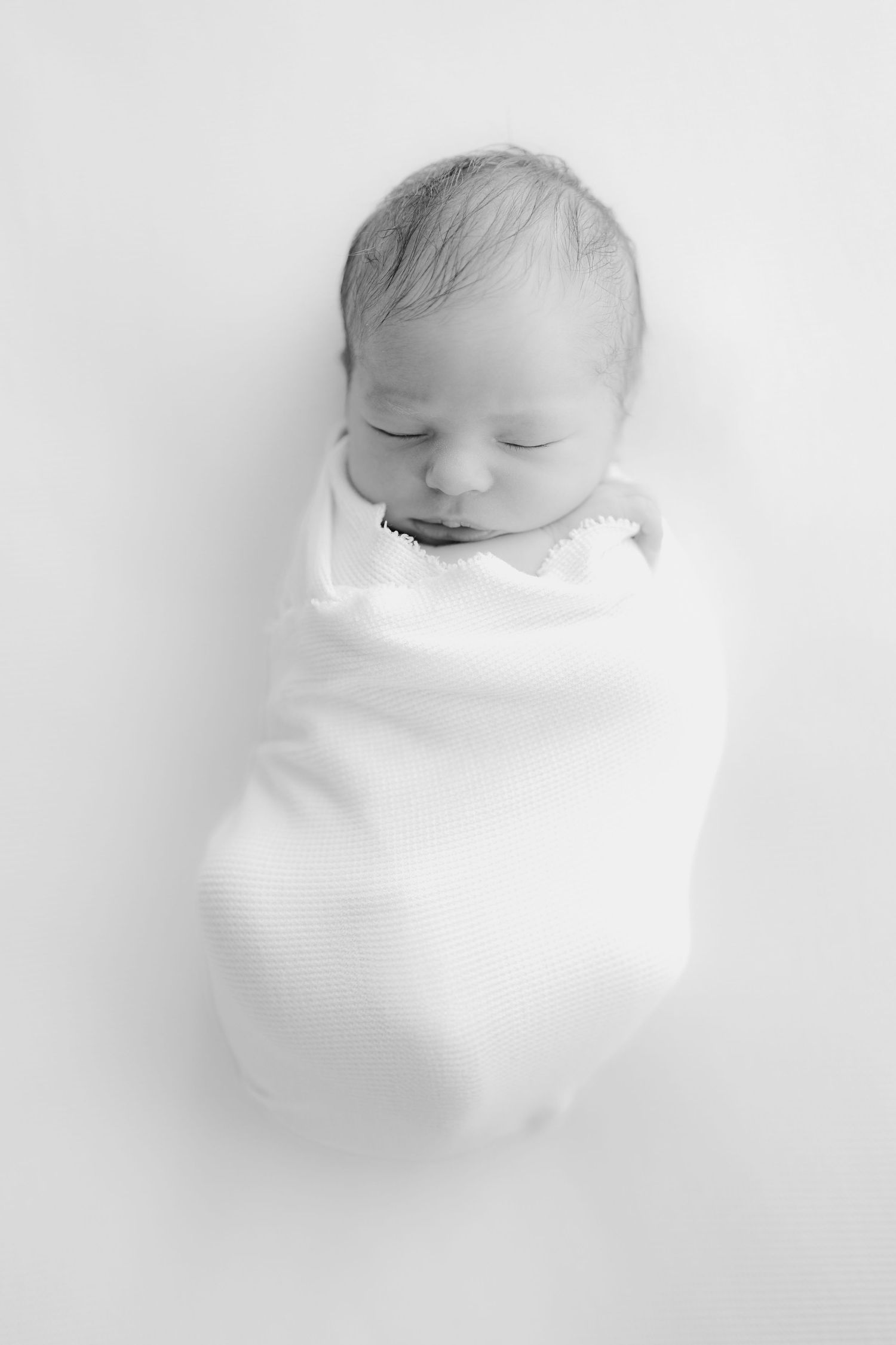 Black and white portrait of peaceful sleeping newborn wrapped in white swaddle.
