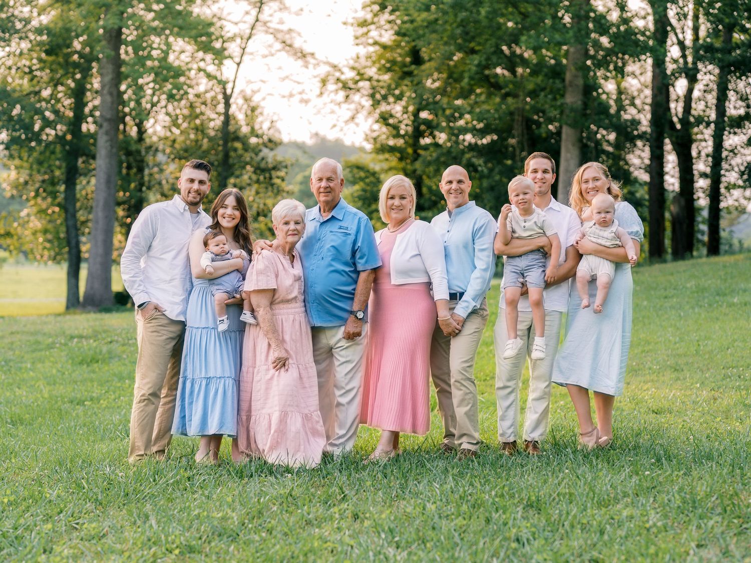 Extended family group portrait outdoors in coordinated pastel outfits.