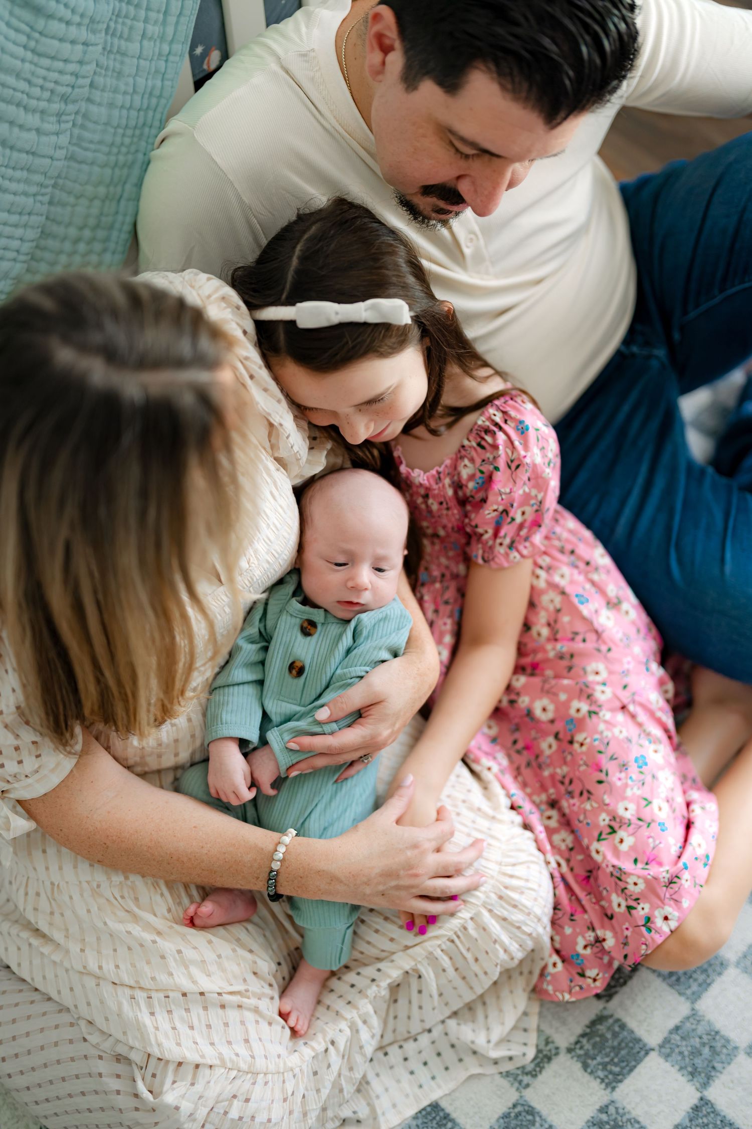 Family members snuggle close together on a checkered blanket while holding a baby.