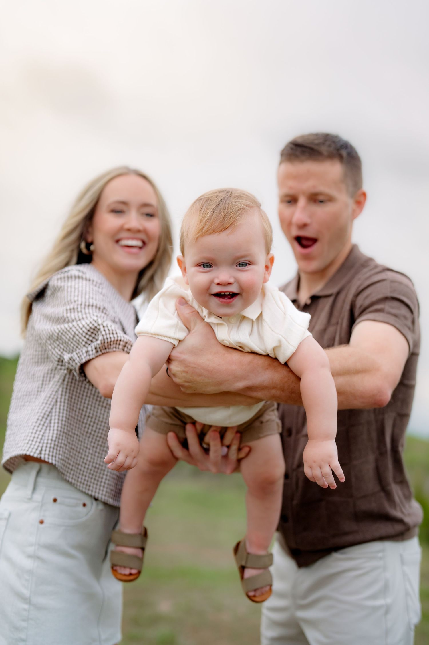 Playful parents lifting laughing baby outdoors.