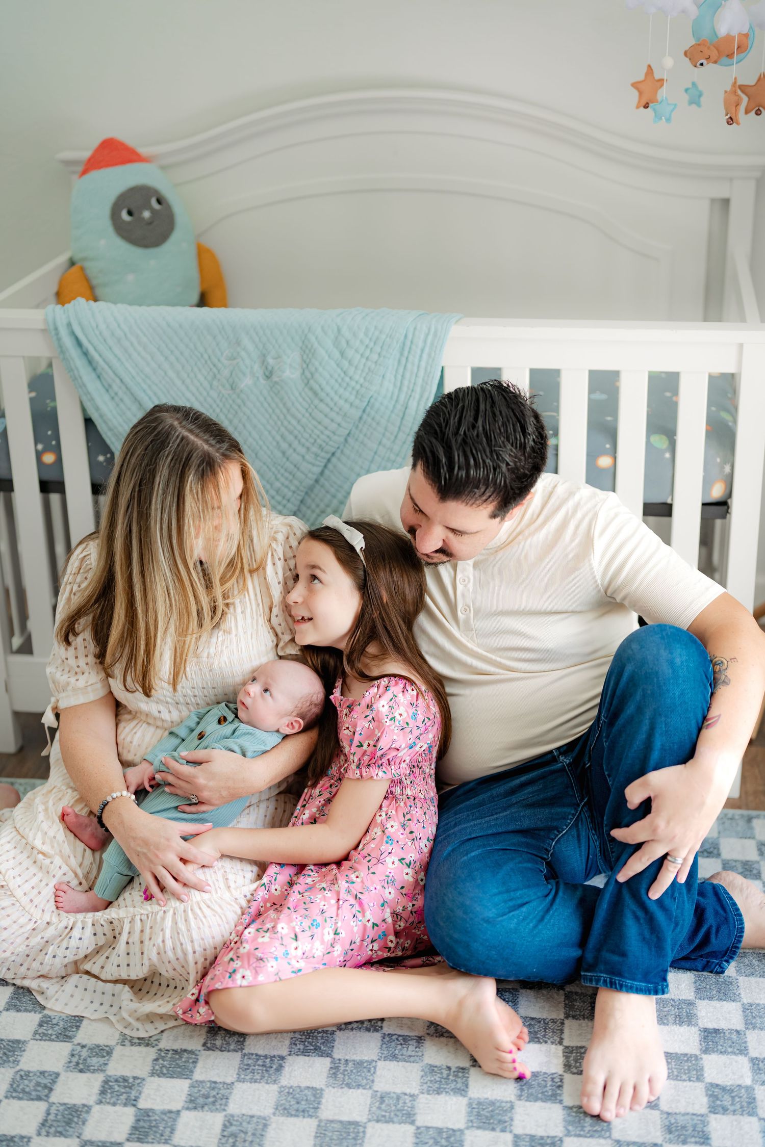 A family shares an intimate moment together on a crib mattress in a nursery with pastel decor.