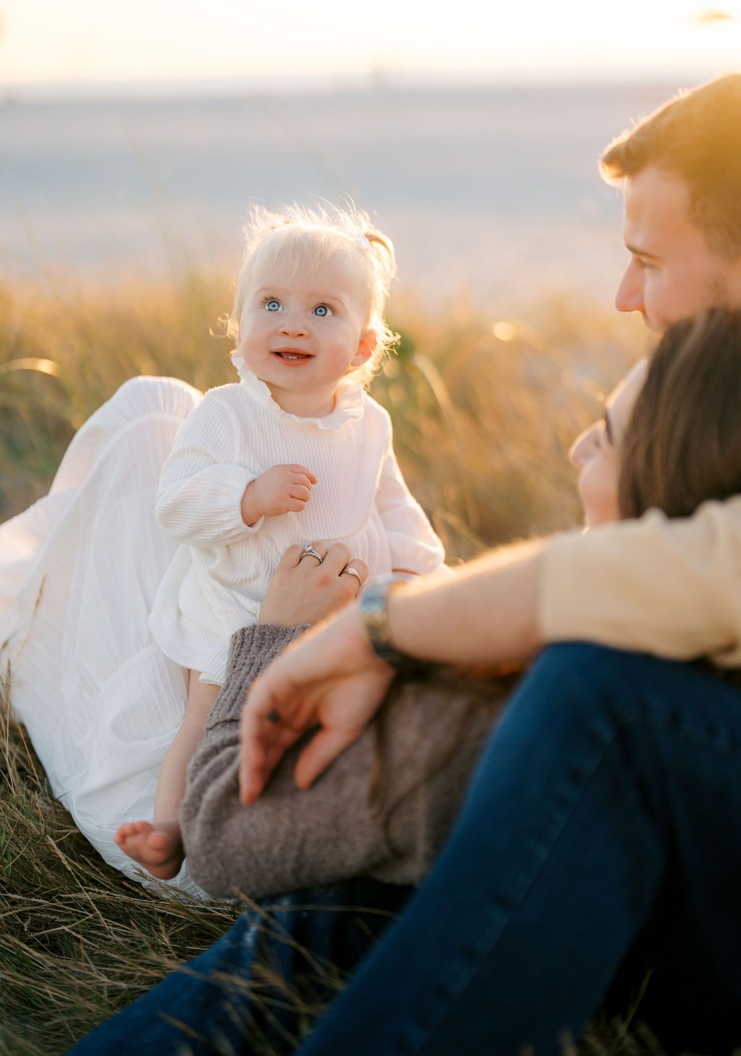 A series of candid outdoor family moments captured during golden hour with a baby in white clothing.