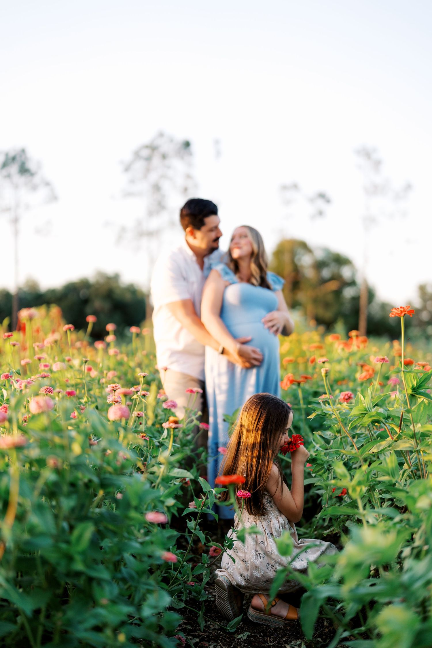 Family poses among colorful wildflowers during outdoor maternity photo session.