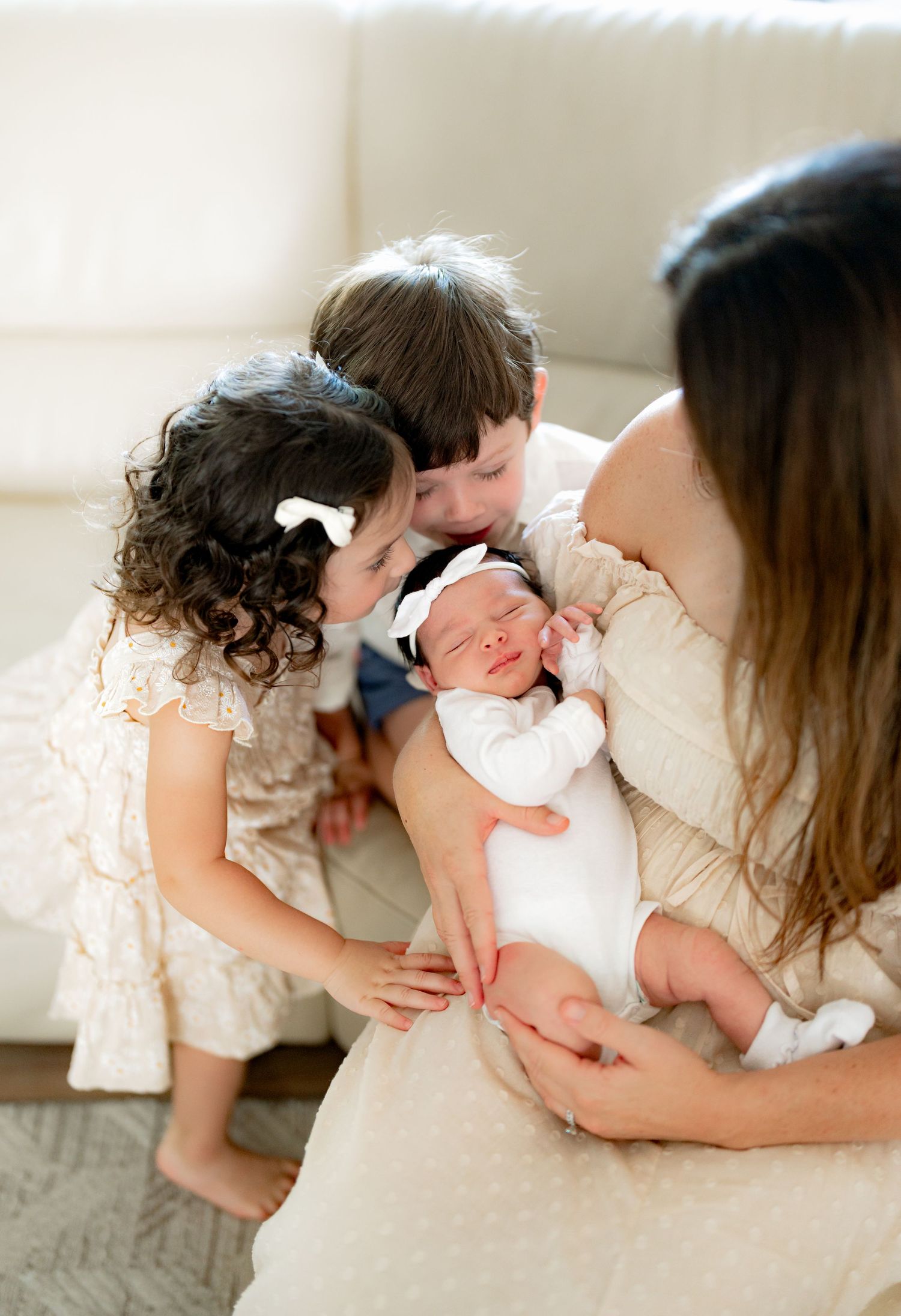 Siblings bonding with newborn baby during lifestyle photo session in white room.