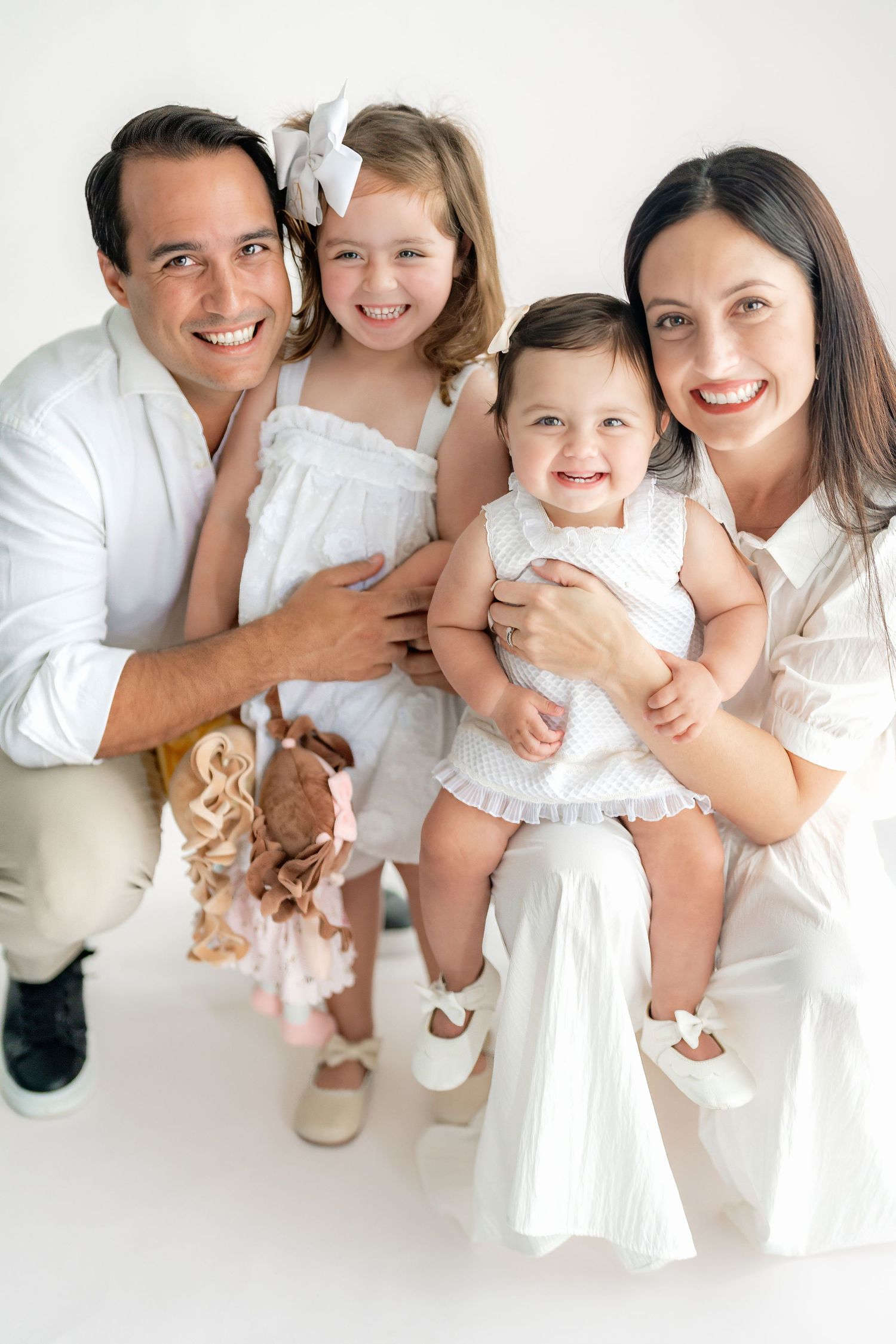 Family dressed in white poses together for studio portrait against white background.