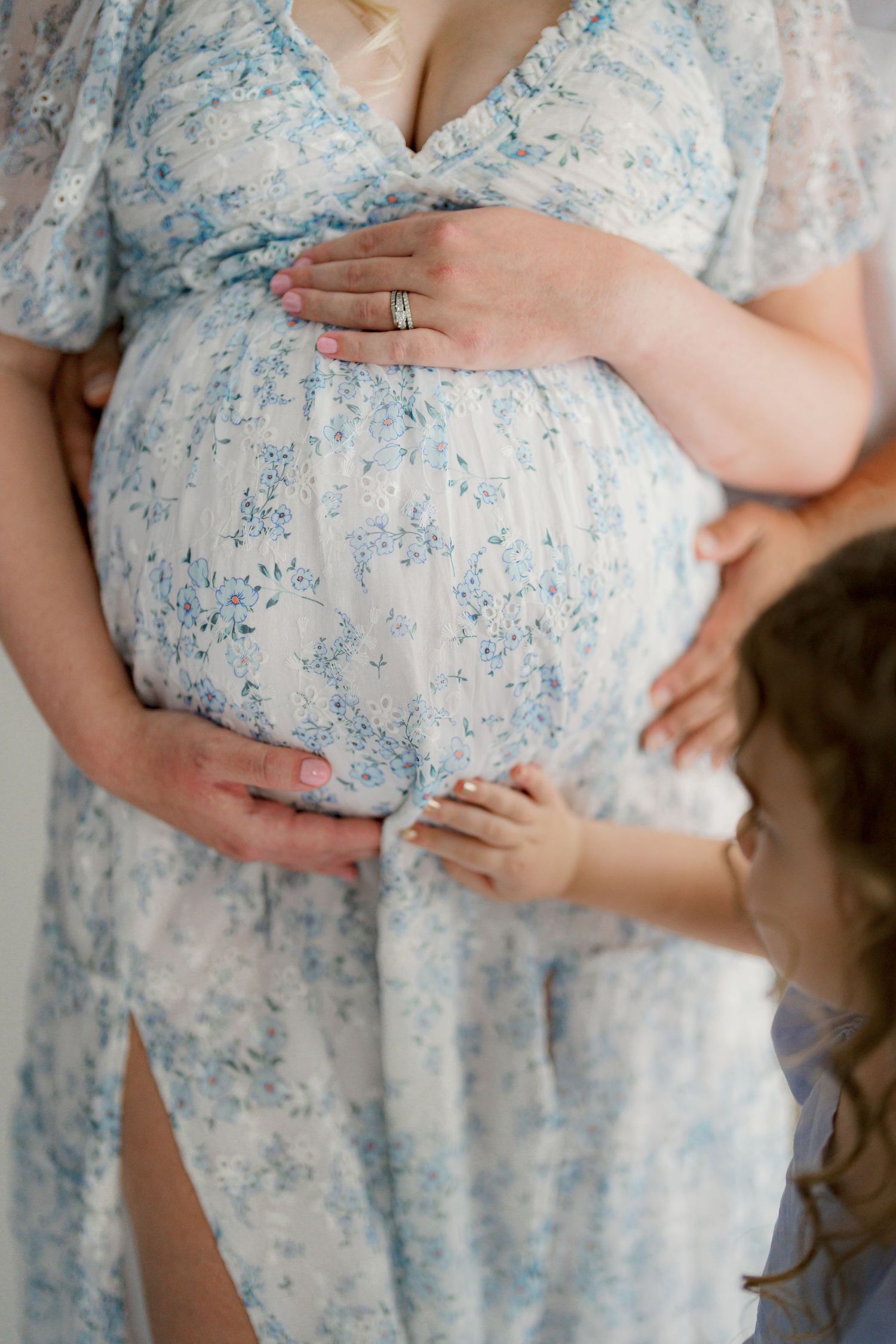 Series of close-up shots showing hands cradling a pregnant belly in a blue floral dress.
