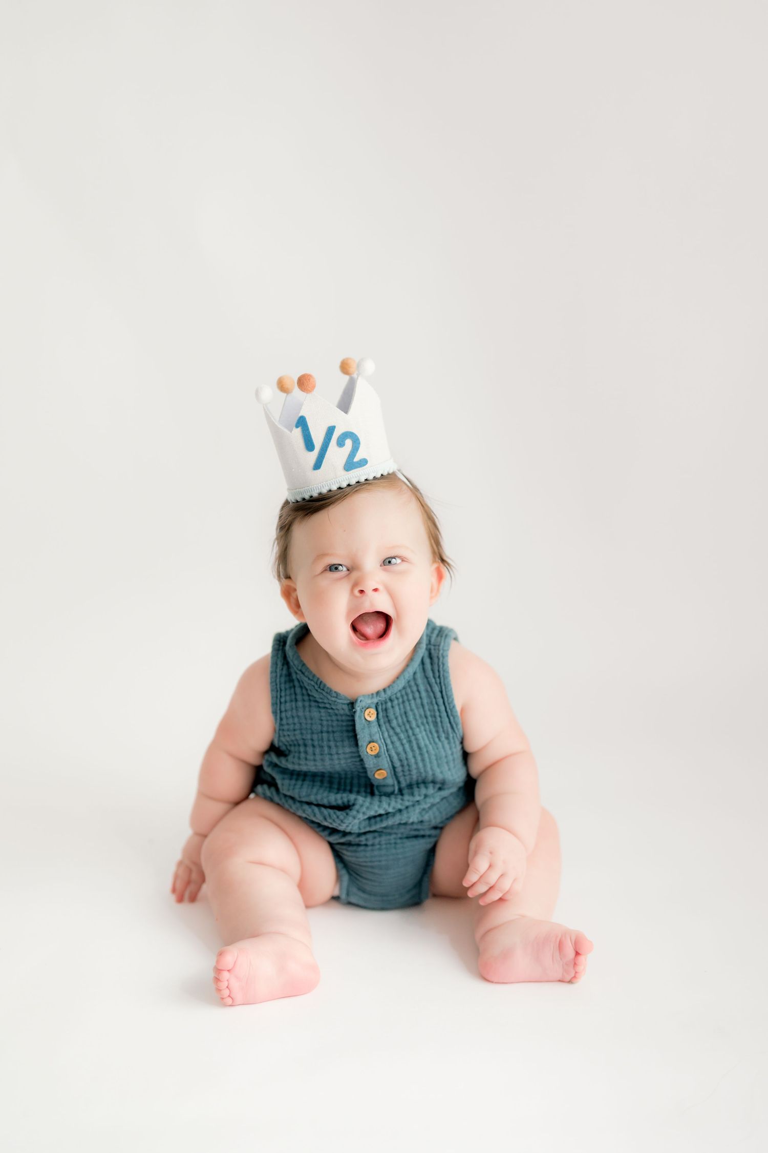 Baby in blue knit romper sits on white background showing playful expressions in three progressive milestone photos.