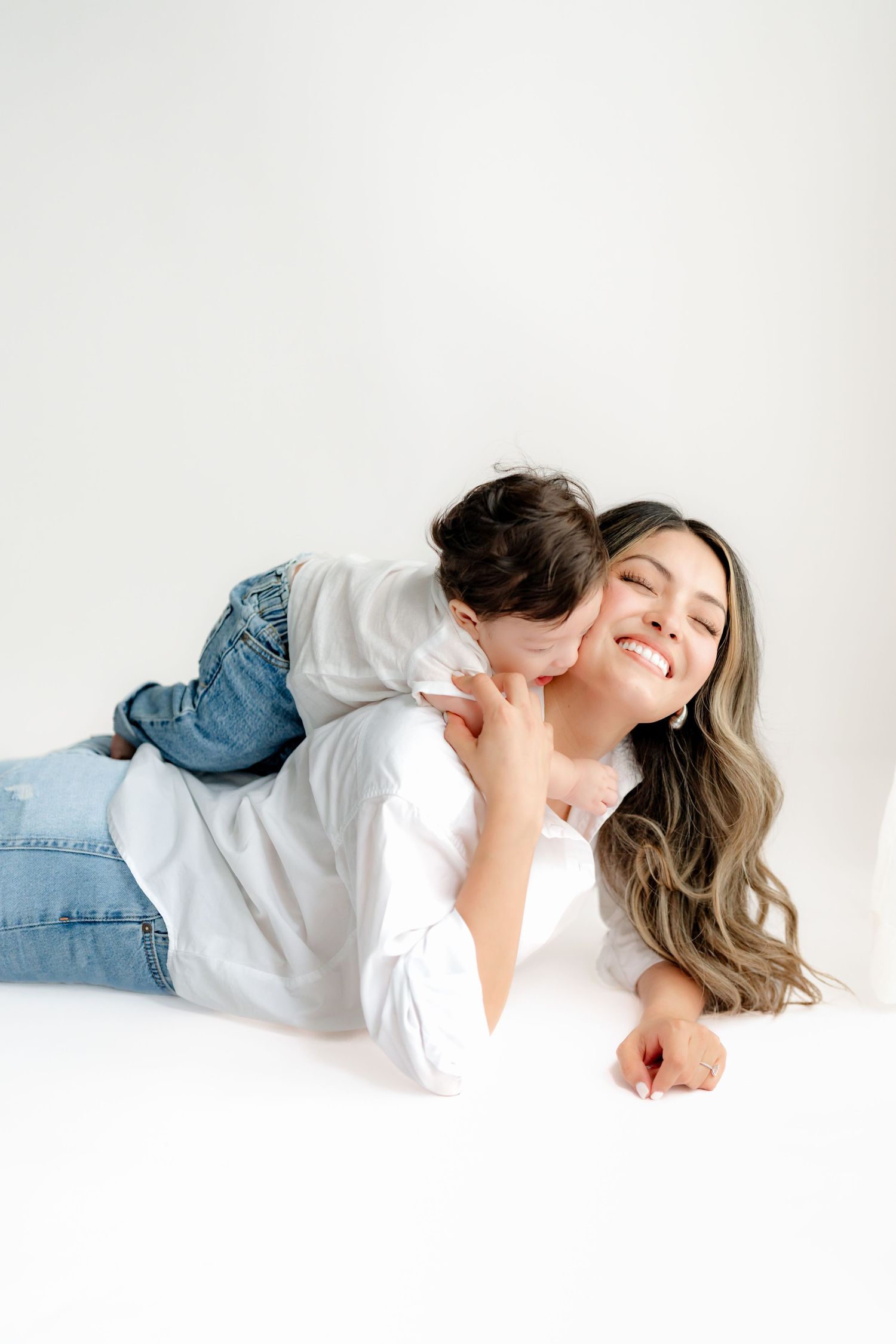 A tender moment captured against white background as parent and child in denim share loving embrace while lying down.