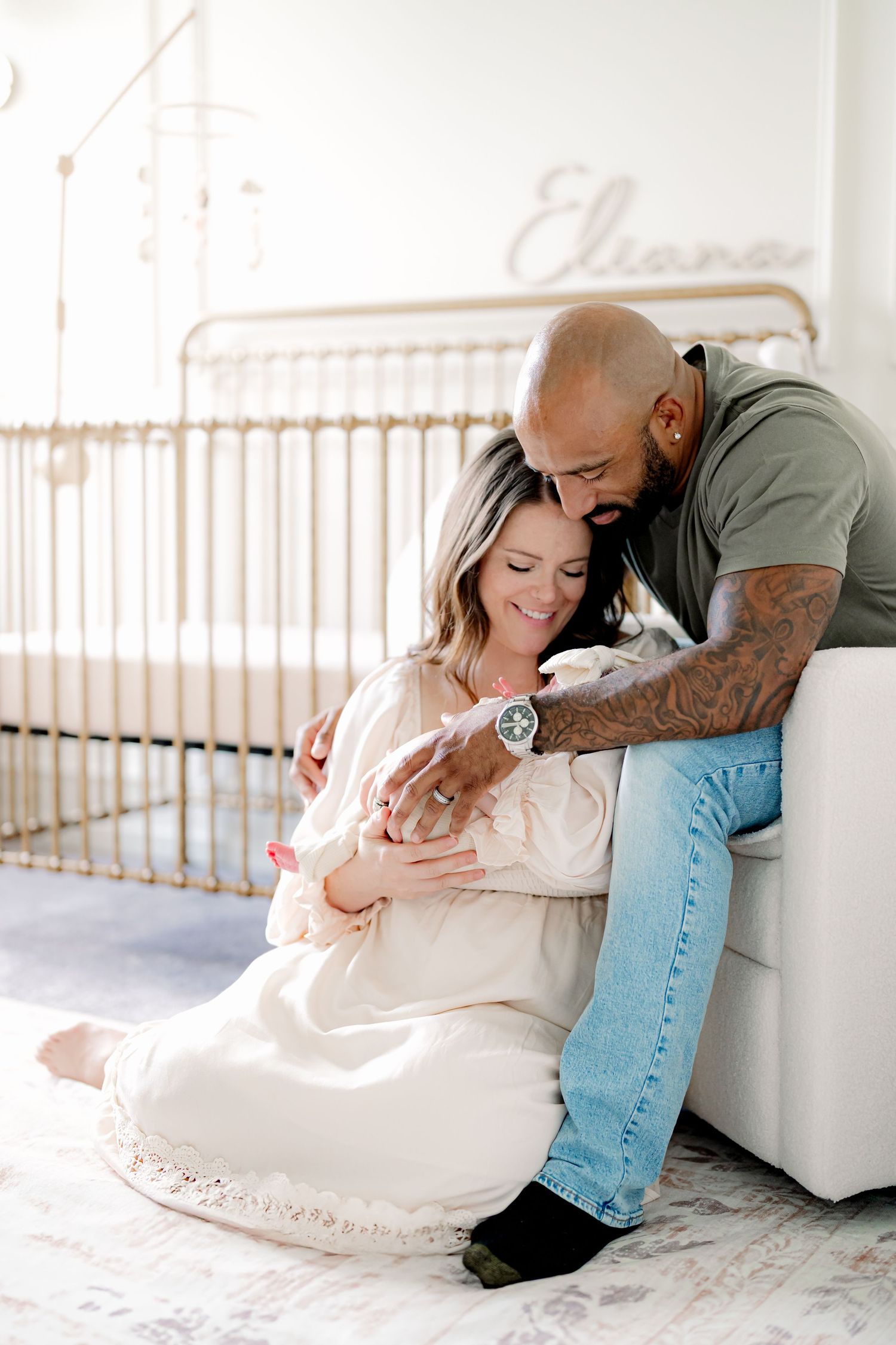 Couple sitting together with newborn by window in bright nursery setting.