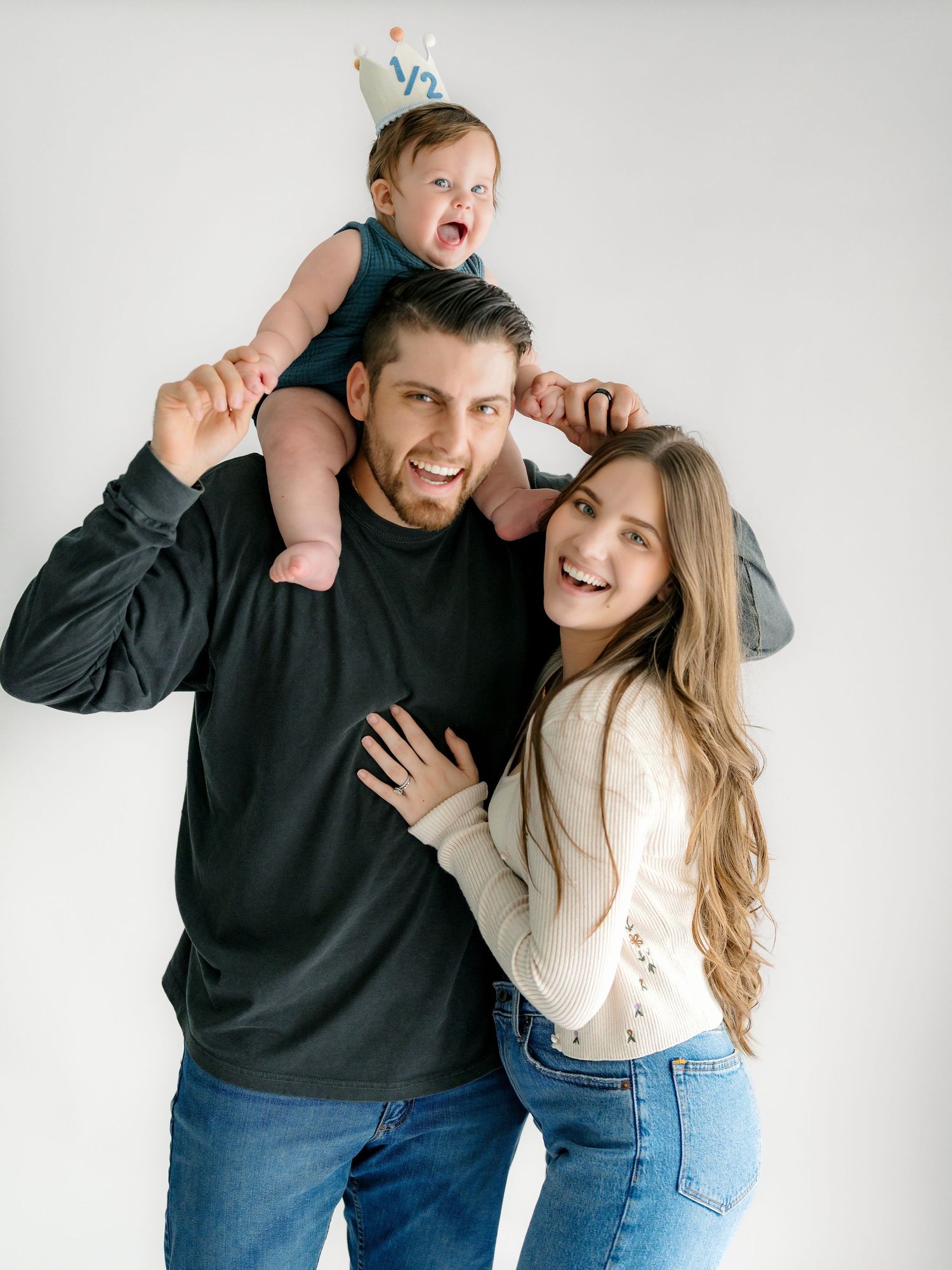 A couple in casual attire laughs and poses playfully together against a white background in a photo series.