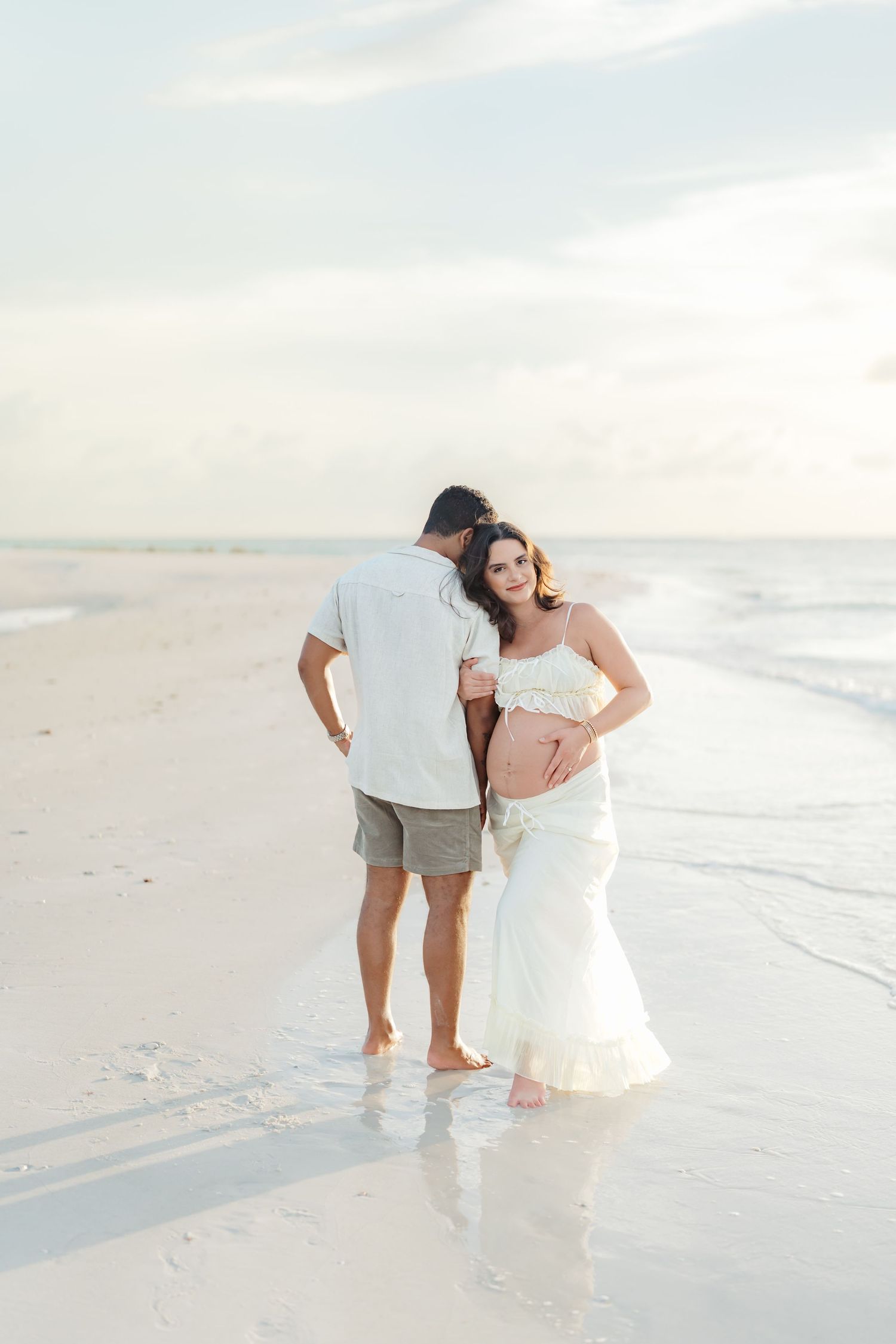 A couple shares a romantic moment walking along a serene white sandy beach at sunset.