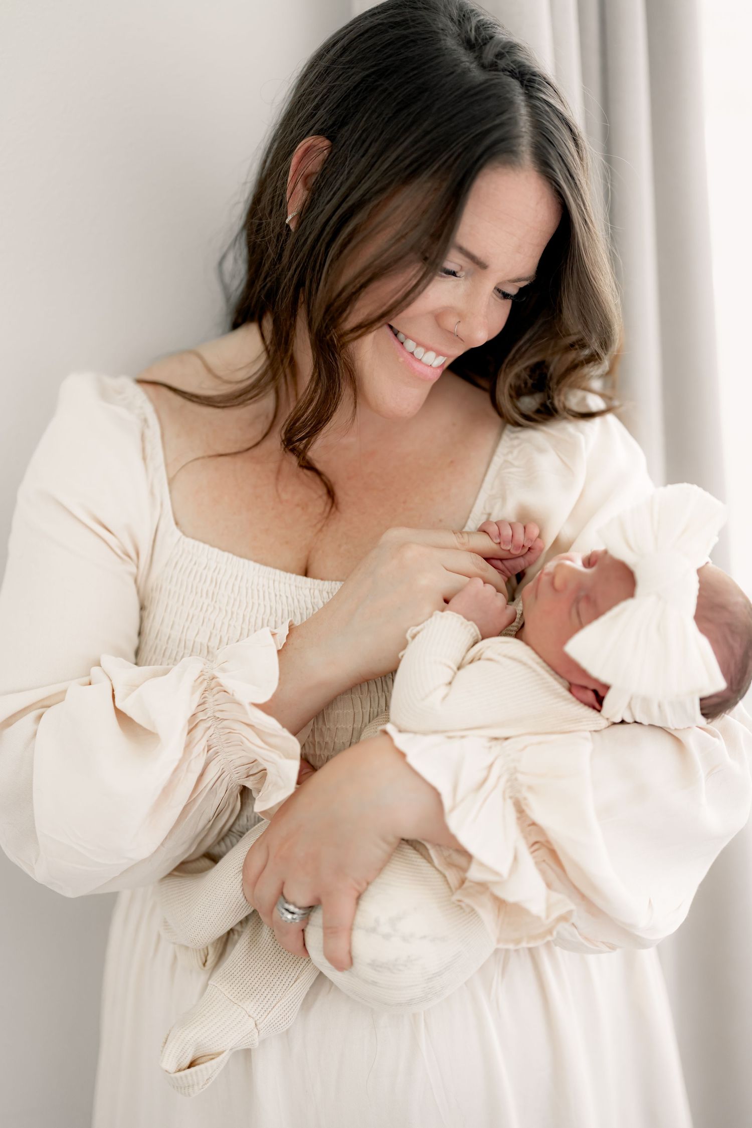Tender moments between parent and newborn in cream colored outfits during indoor photo session.