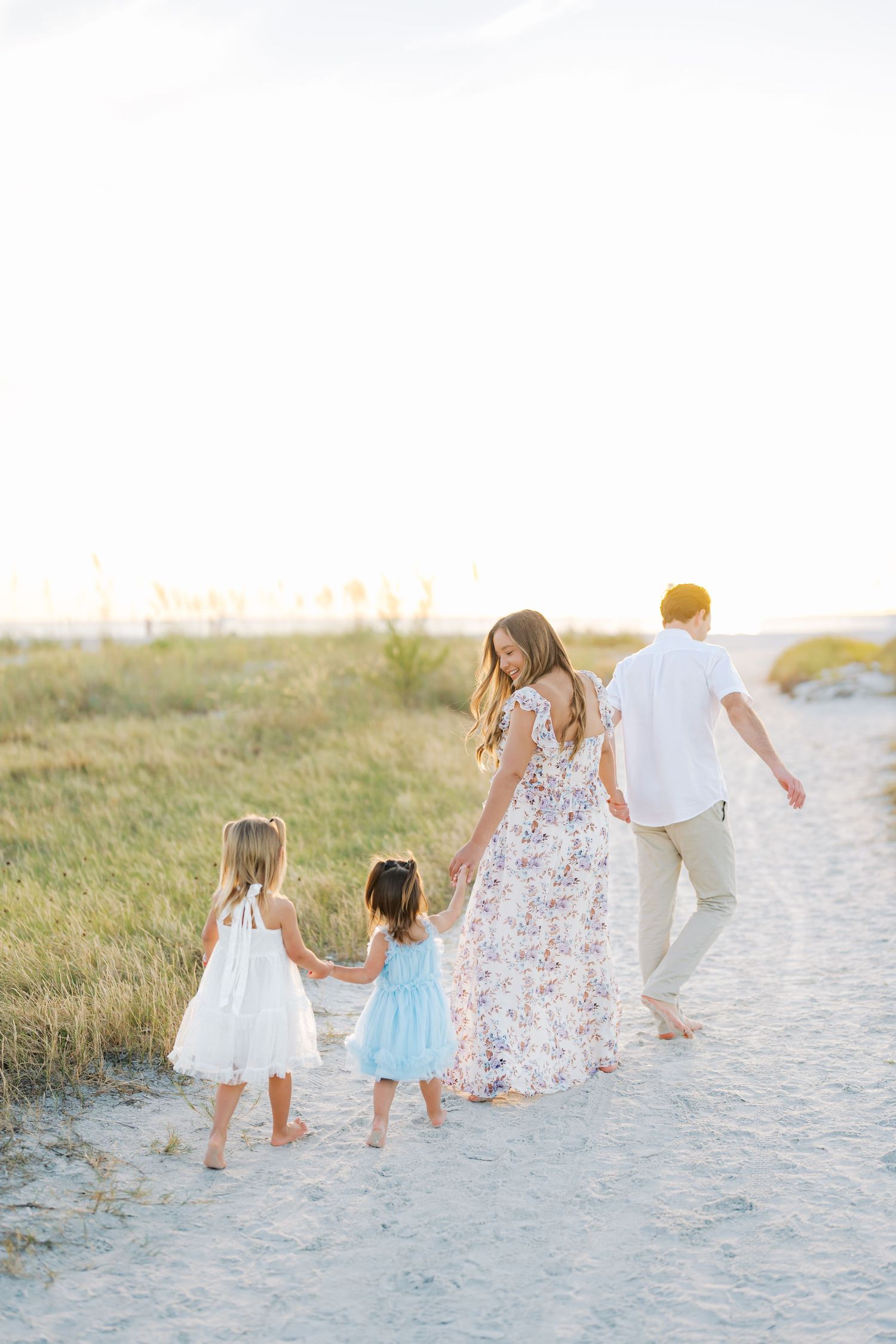 Family walking together on sandy beach path at sunset wearing coordinated white and floral outfits.