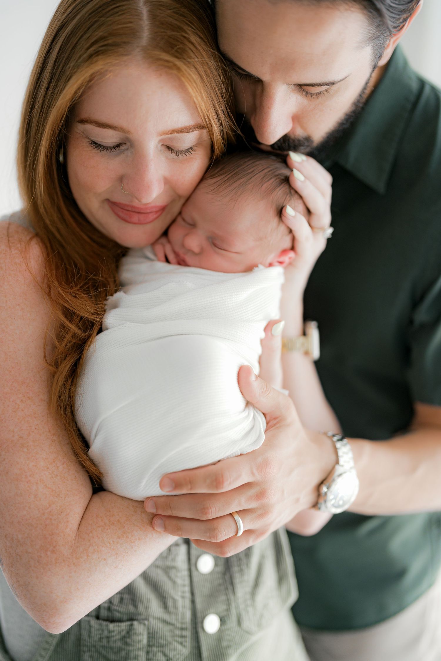 A couple shares a tender moment with their newborn baby wrapped in white.