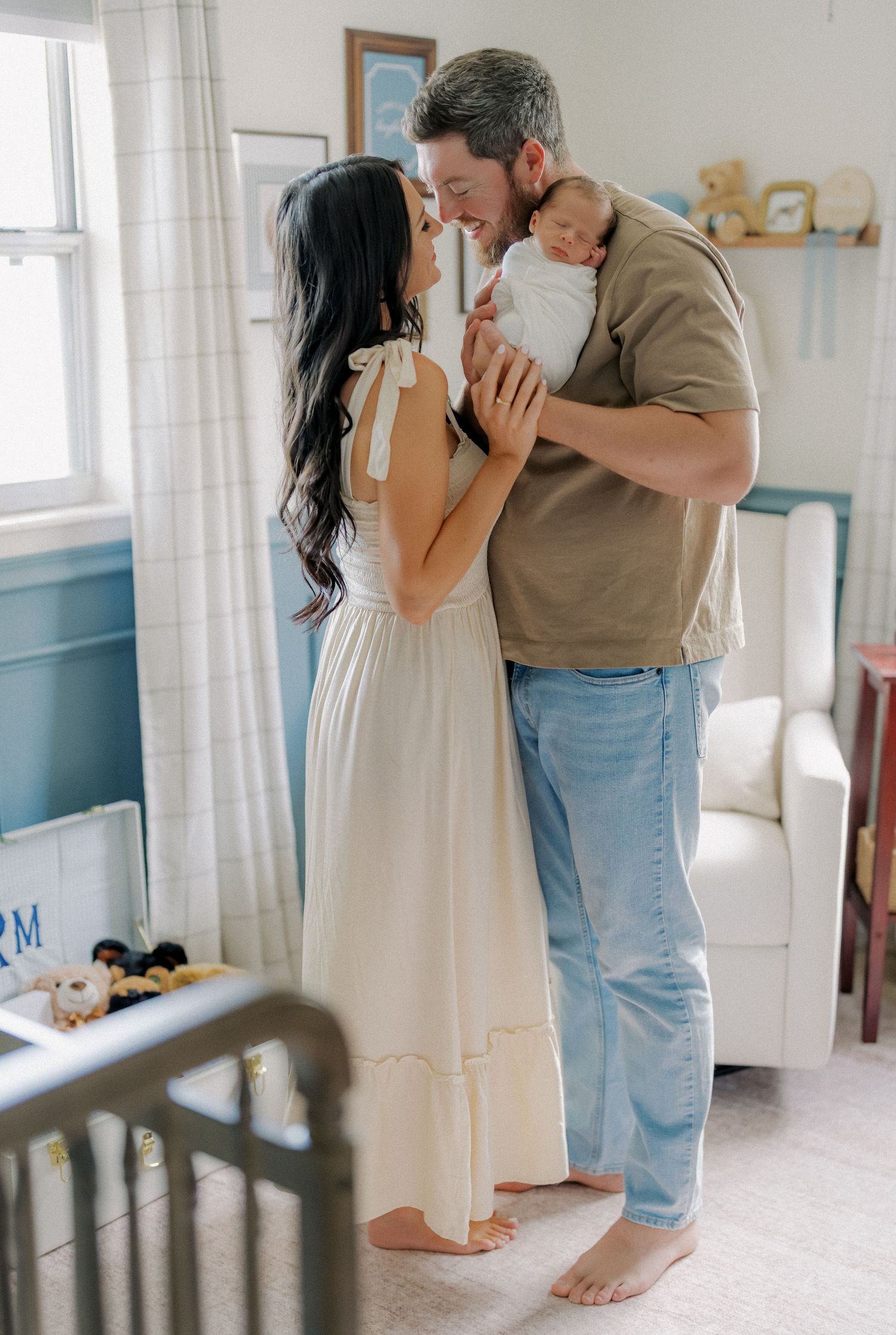 New parents sharing a tender moment with their swaddled newborn baby in a softly decorated nursery room.