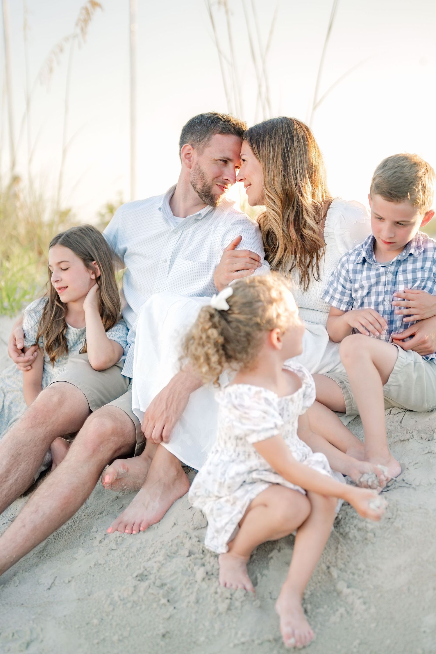Family sitting together on sandy beach dunes at golden hour.