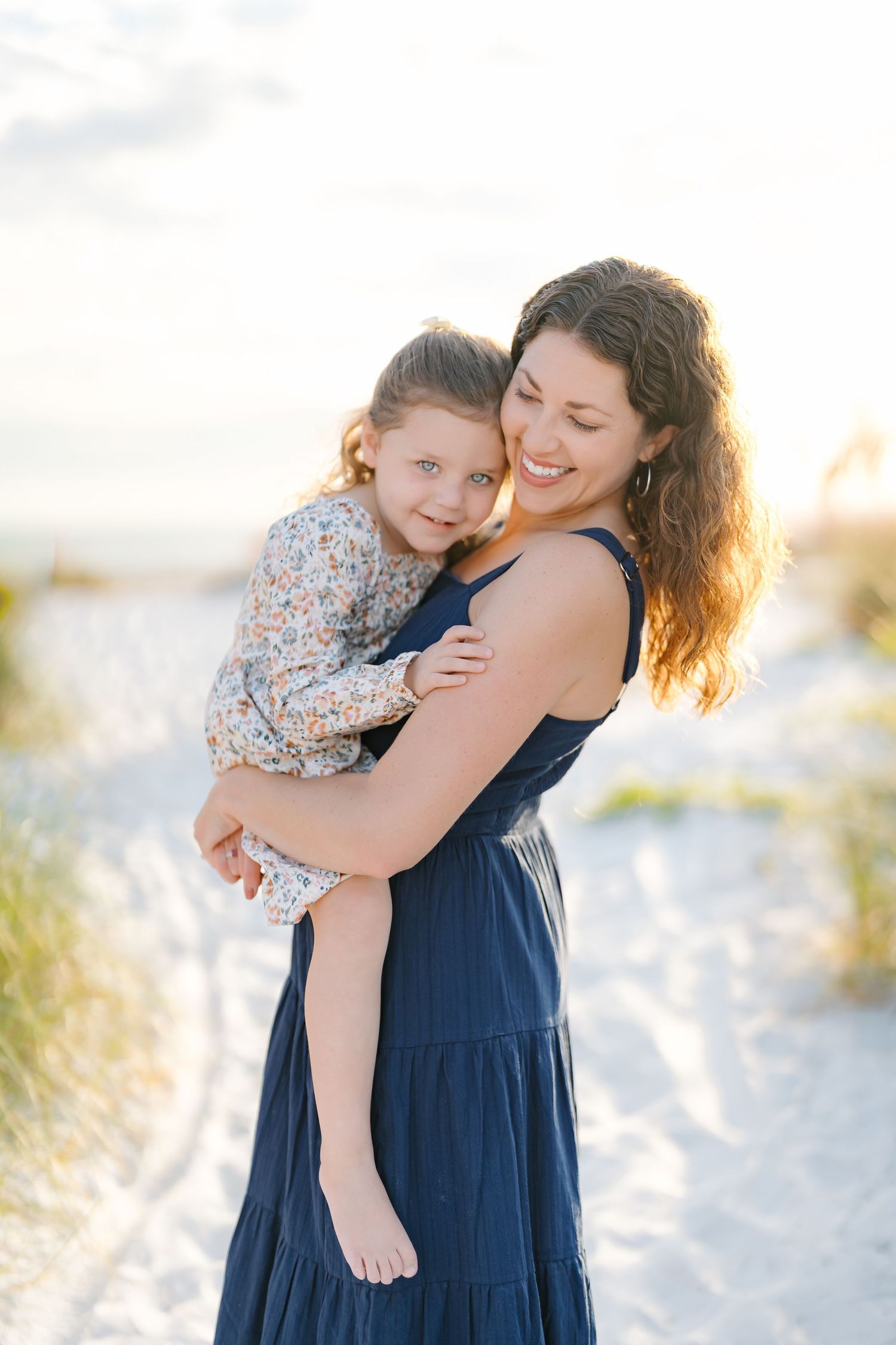 A tender embrace between parent and child on a sunny beach with white sand and soft golden light.