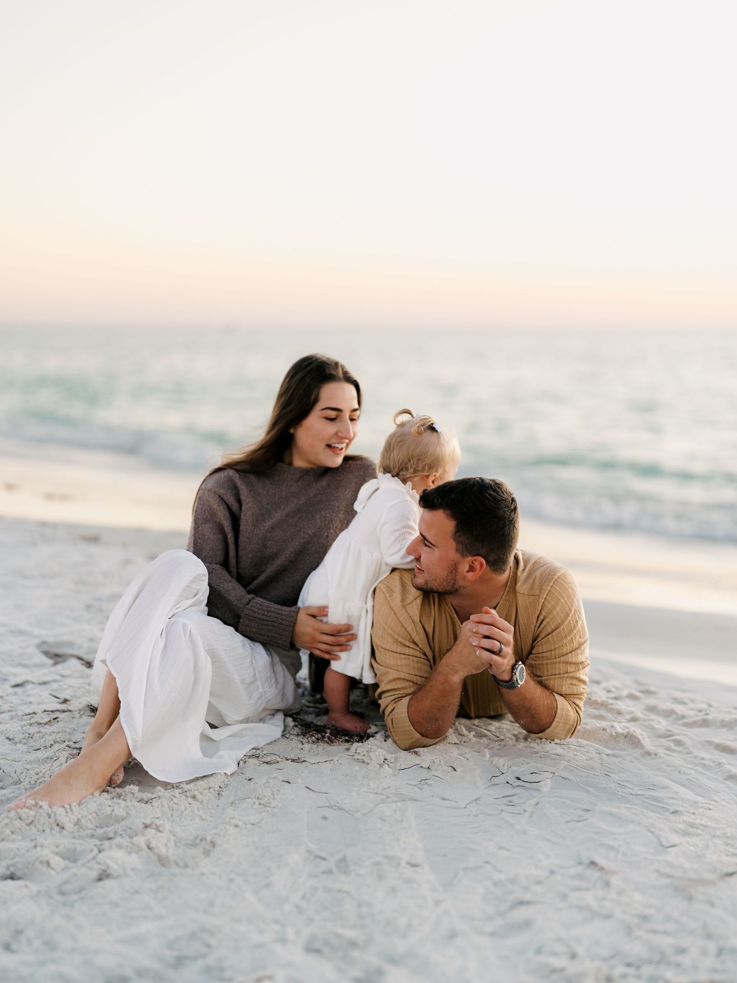 A couple lying on a sandy beach during sunset sharing intimate moments in a series of romantic poses.