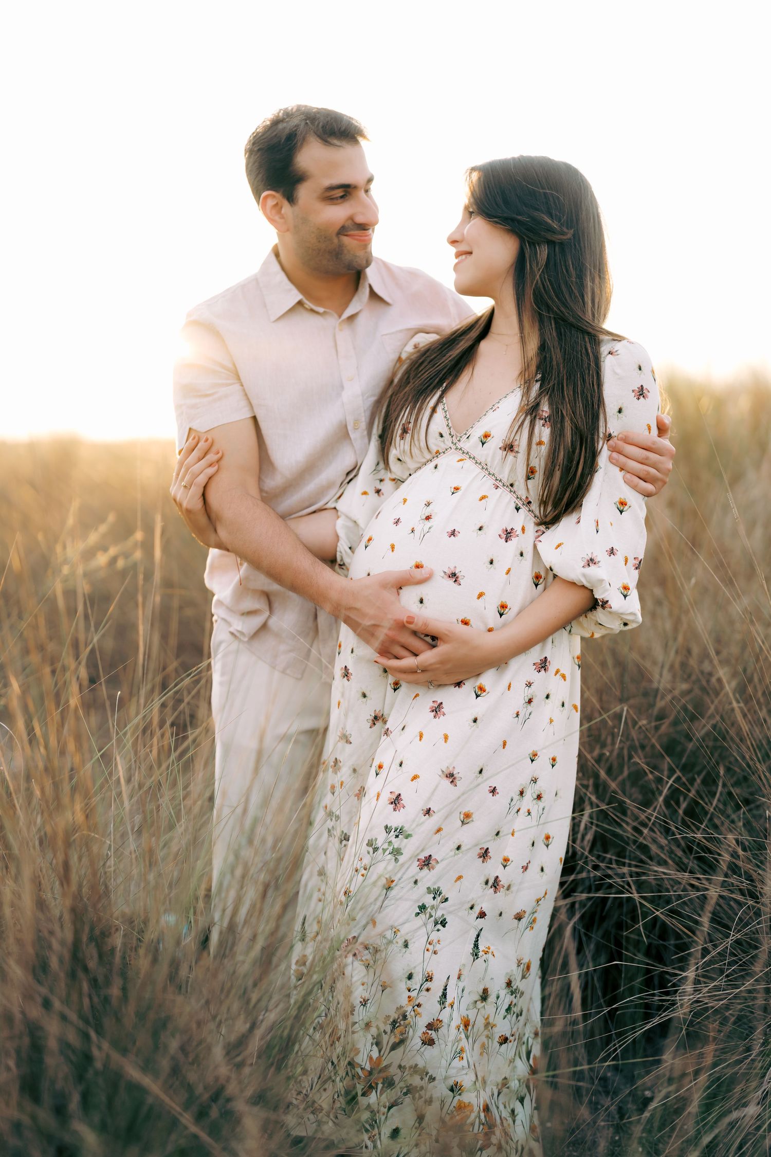 Romantic maternity photos of couple embracing in field during golden hour.