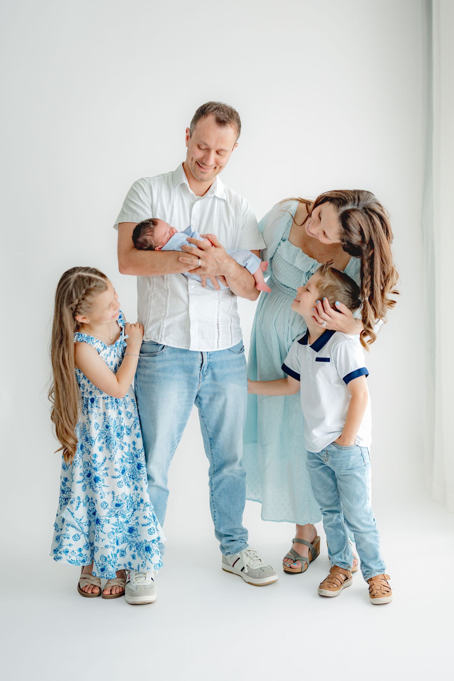 A family in coordinated blue and white outfits shares playful moment against white backdrop.