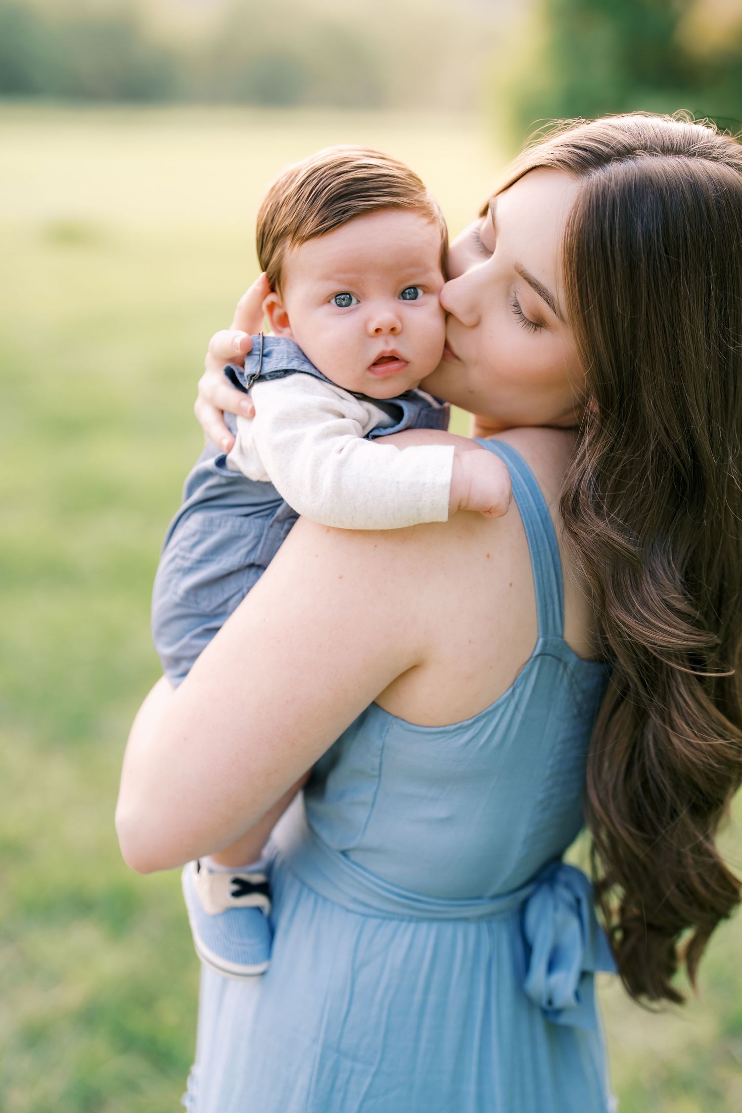 Tender moment between parent and baby in blue dress against blurred green background.