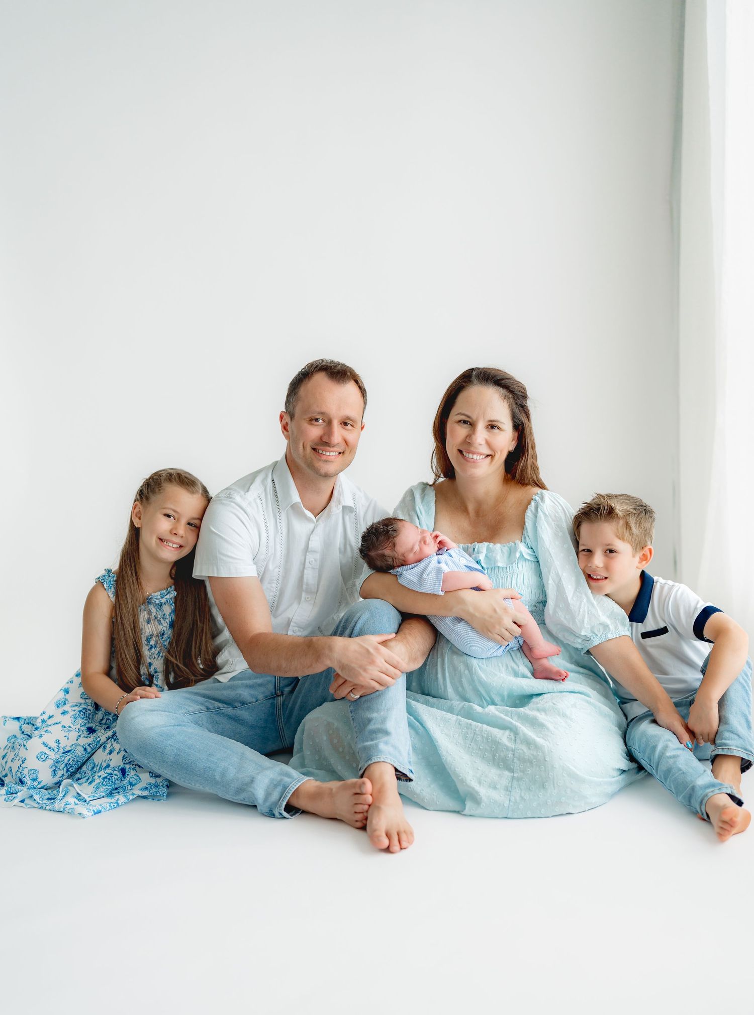Family group wearing coordinating blue outfits resting on white floor during photo session.