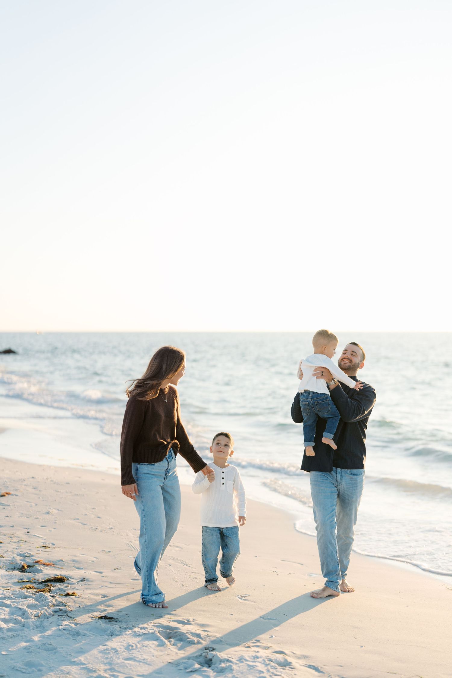 Family walking together on a sandy beach at sunset while holding hands and enjoying quality time by the ocean.