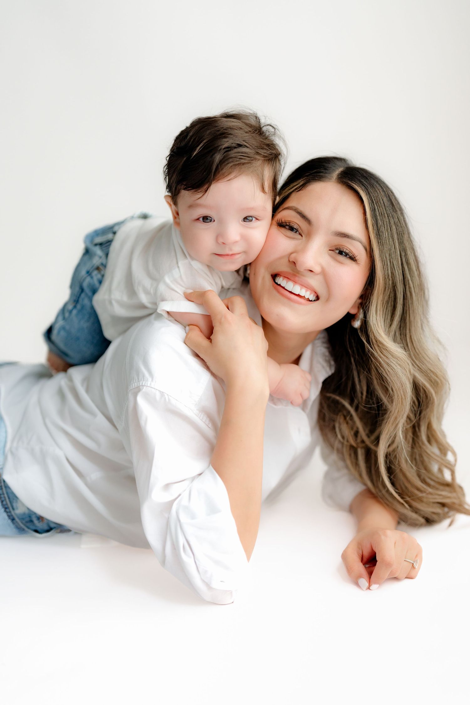 A parent and young child in matching white tops and jeans pose together on a white background for a casual portrait.
