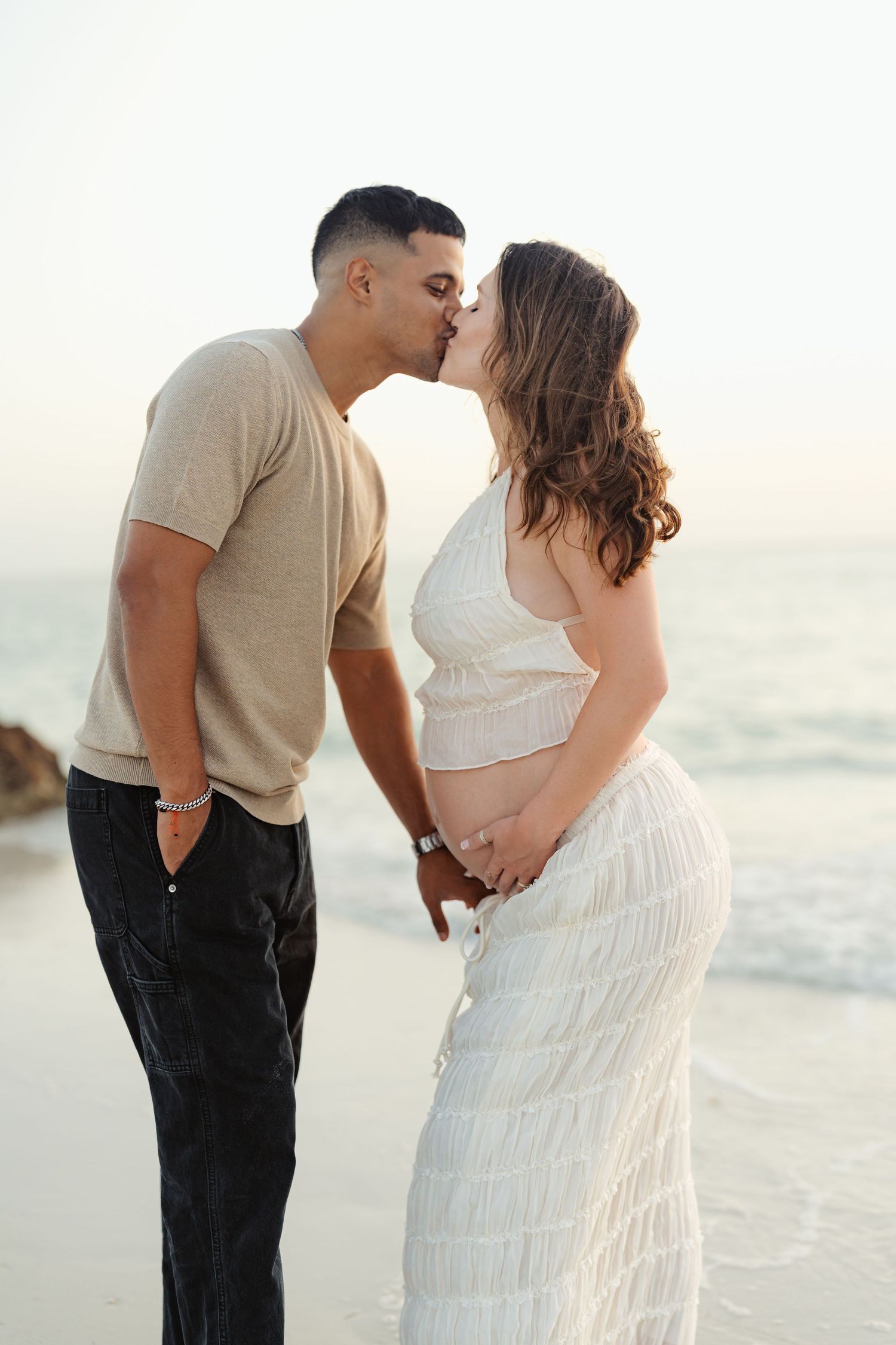 Intimate beachside maternity photos with couple in white dress and casual wear.