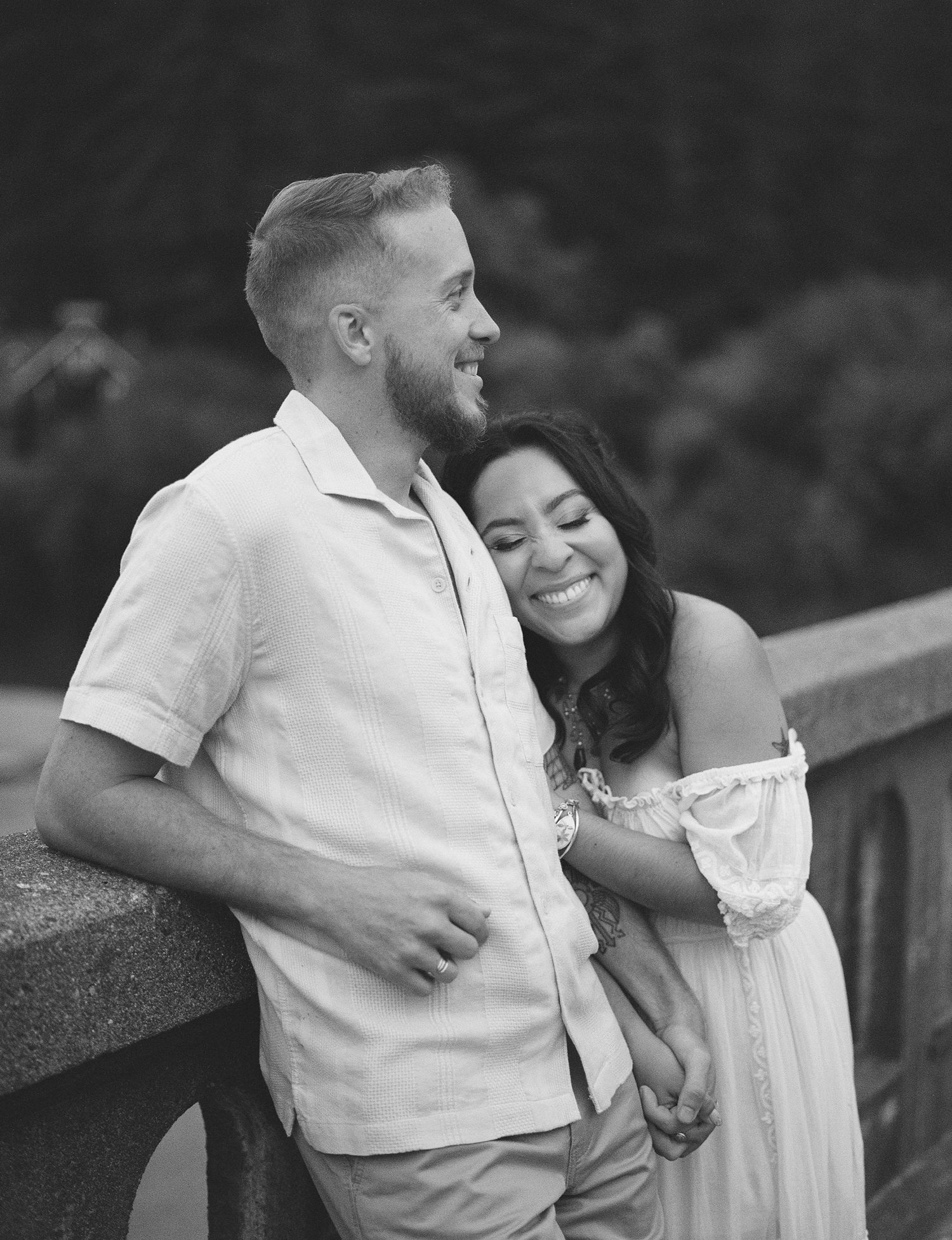 A couple shares a romantic moment together on a bridge in black and white photography.