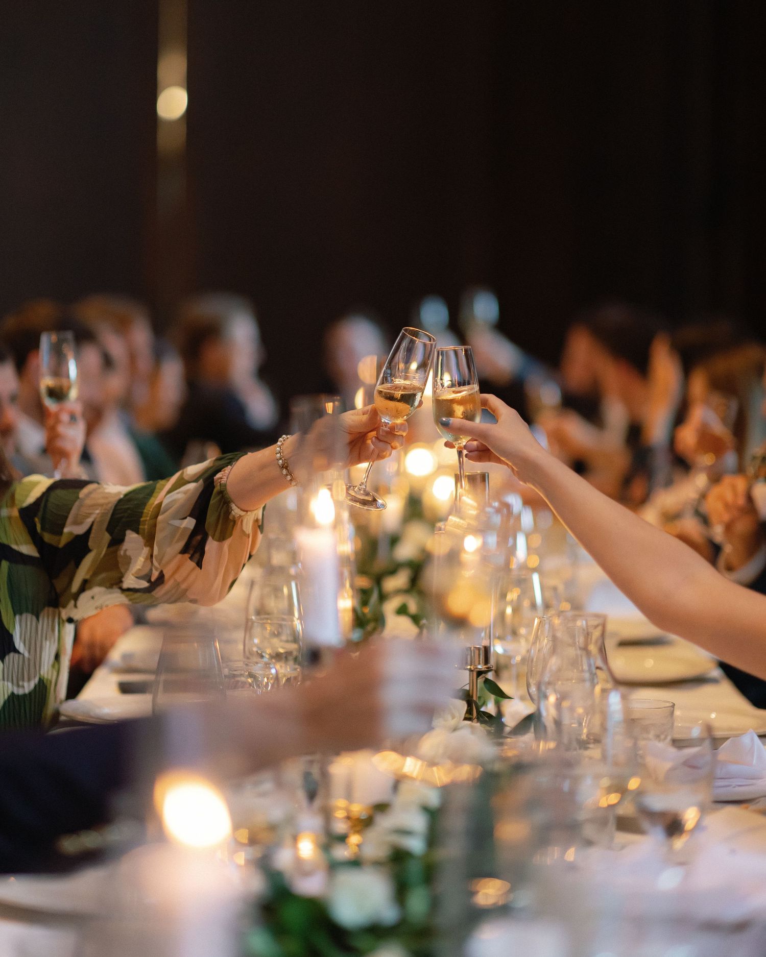 Wedding guests raising champagne glasses for a toast at an elegantly set dinner table.